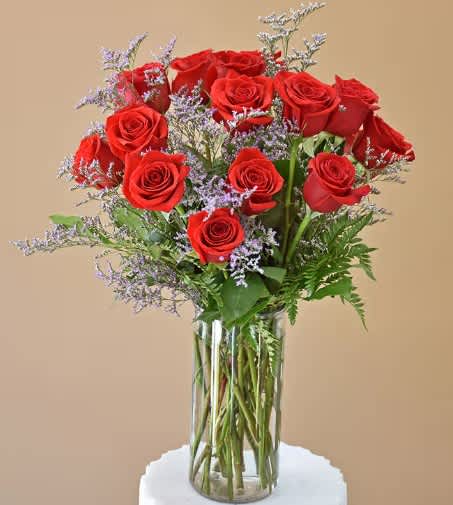 Red roses arranged in a clear glass vase with purple filler flowers