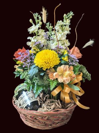 Basket arrangement with yellow and peach flowers and a wine bottle