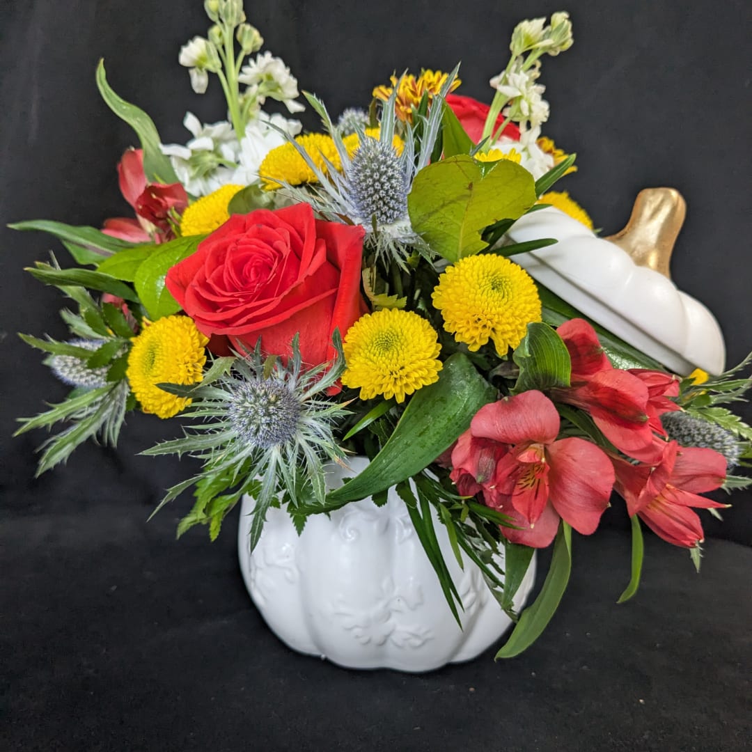 Mixed bouquet with red roses, yellow mums, and pink flowers in a white pumpkin vase