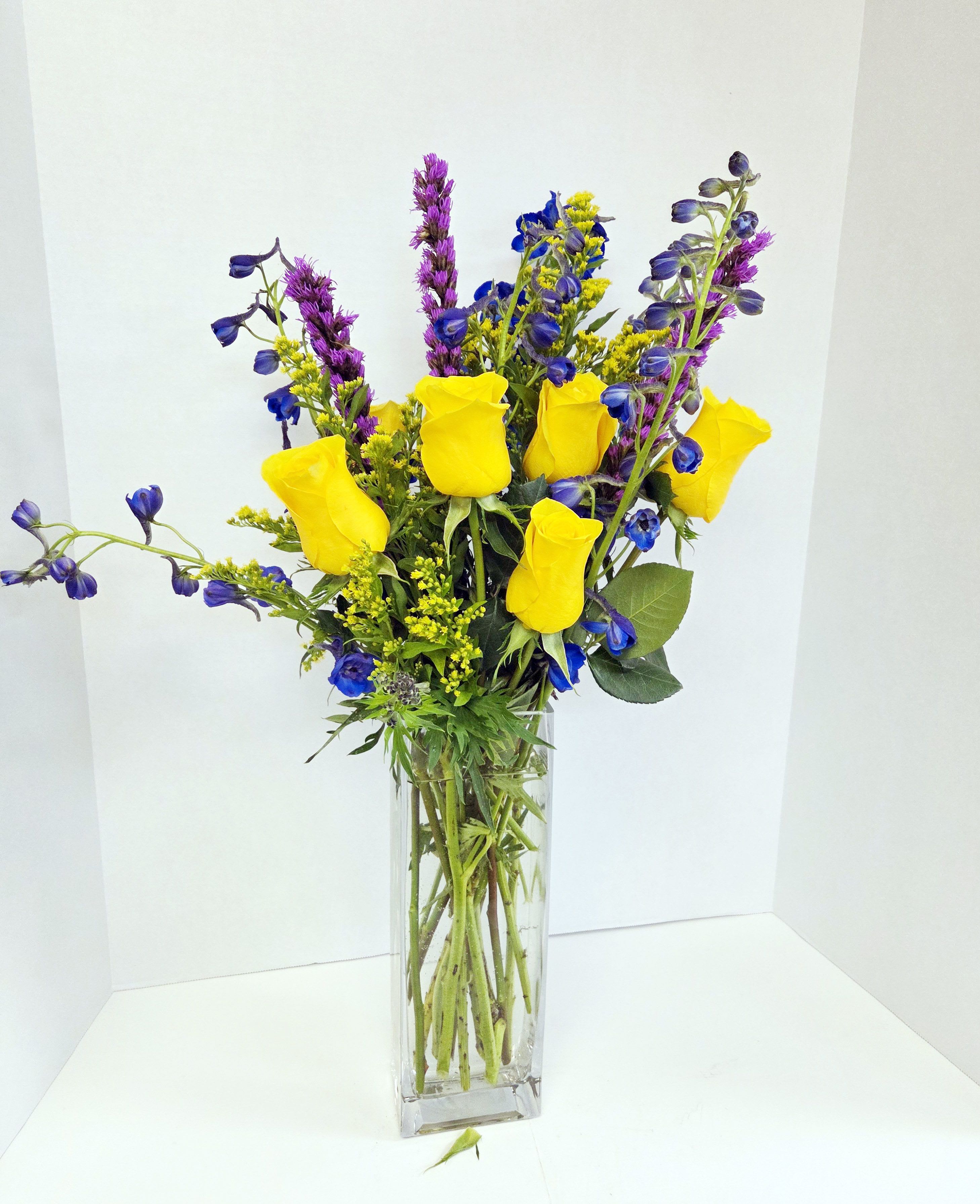 Yellow roses and blue-purple flowers in a clear glass vase