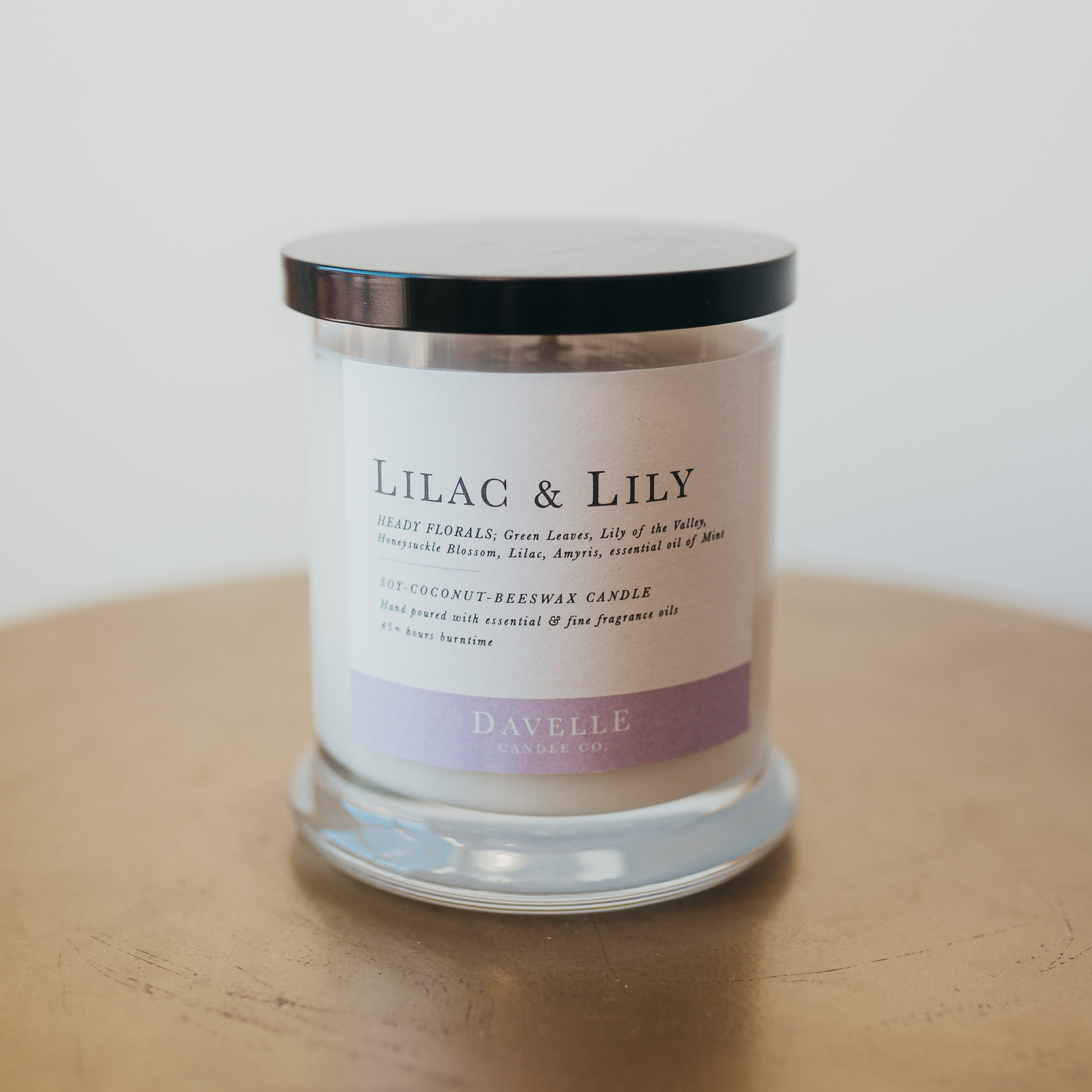 A lilac and lily scented candle in a glass jar with a black lid