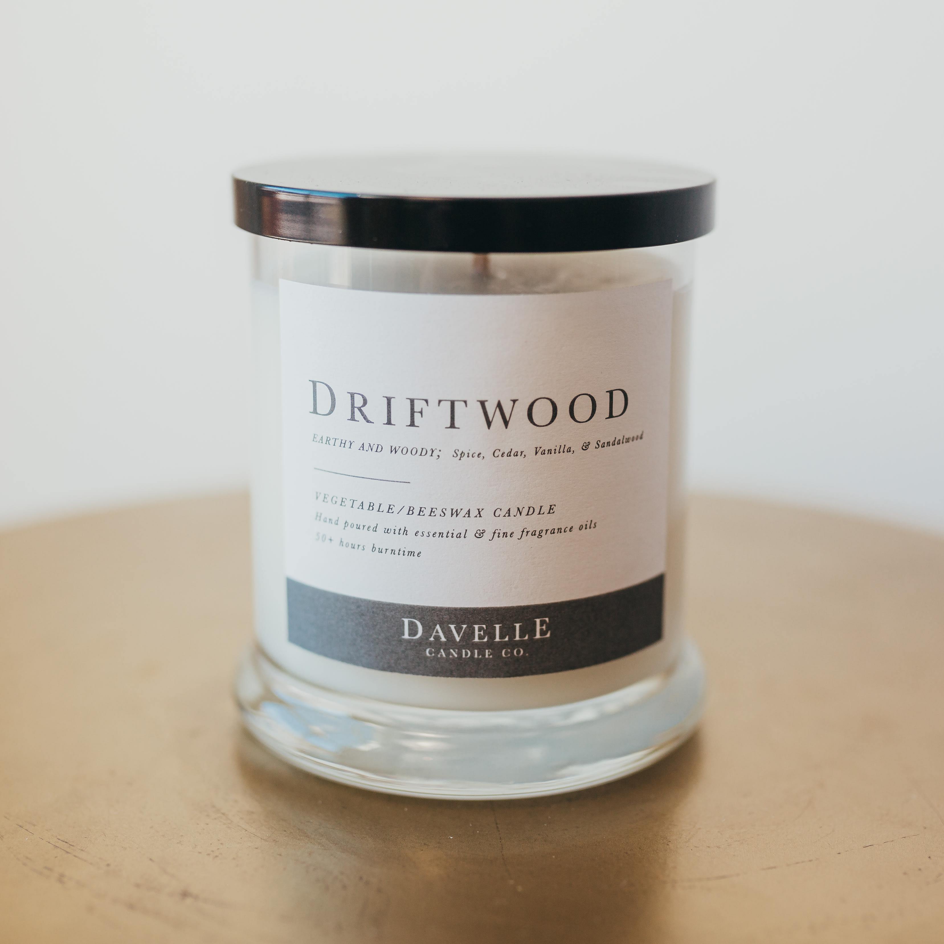 A driftwood-scented candle in a clear glass jar with a black lid