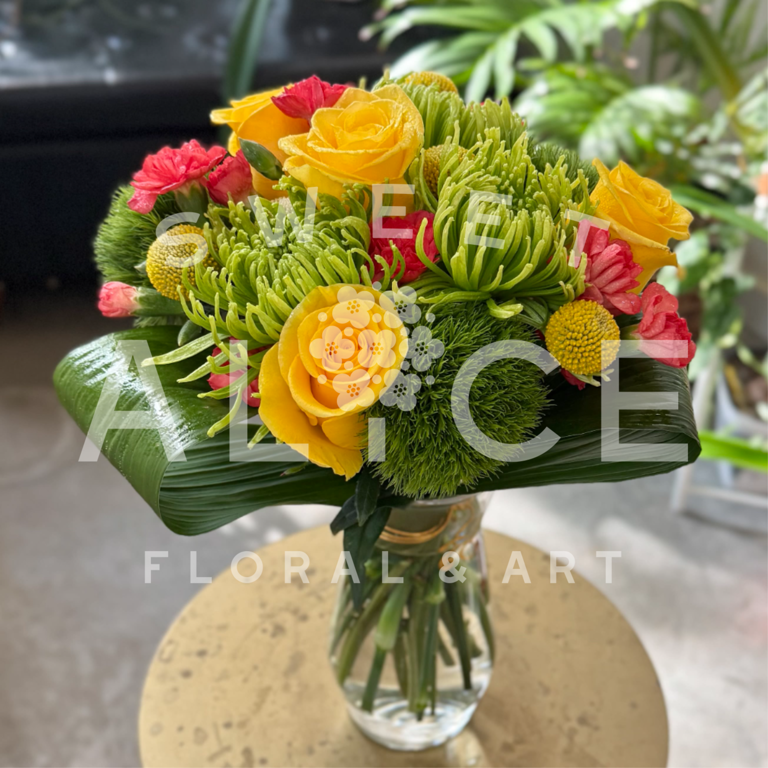 Bright bouquet of yellow roses and green mums with pink blooms in a clear glass vase