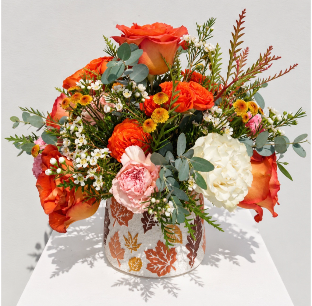 Orange roses and mixed blooms in a leaf-patterned vase