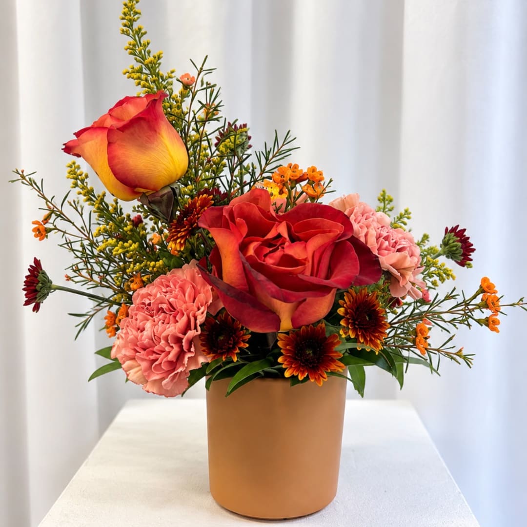 Bouquet of red and yellow roses with pink carnations in a tan vase
