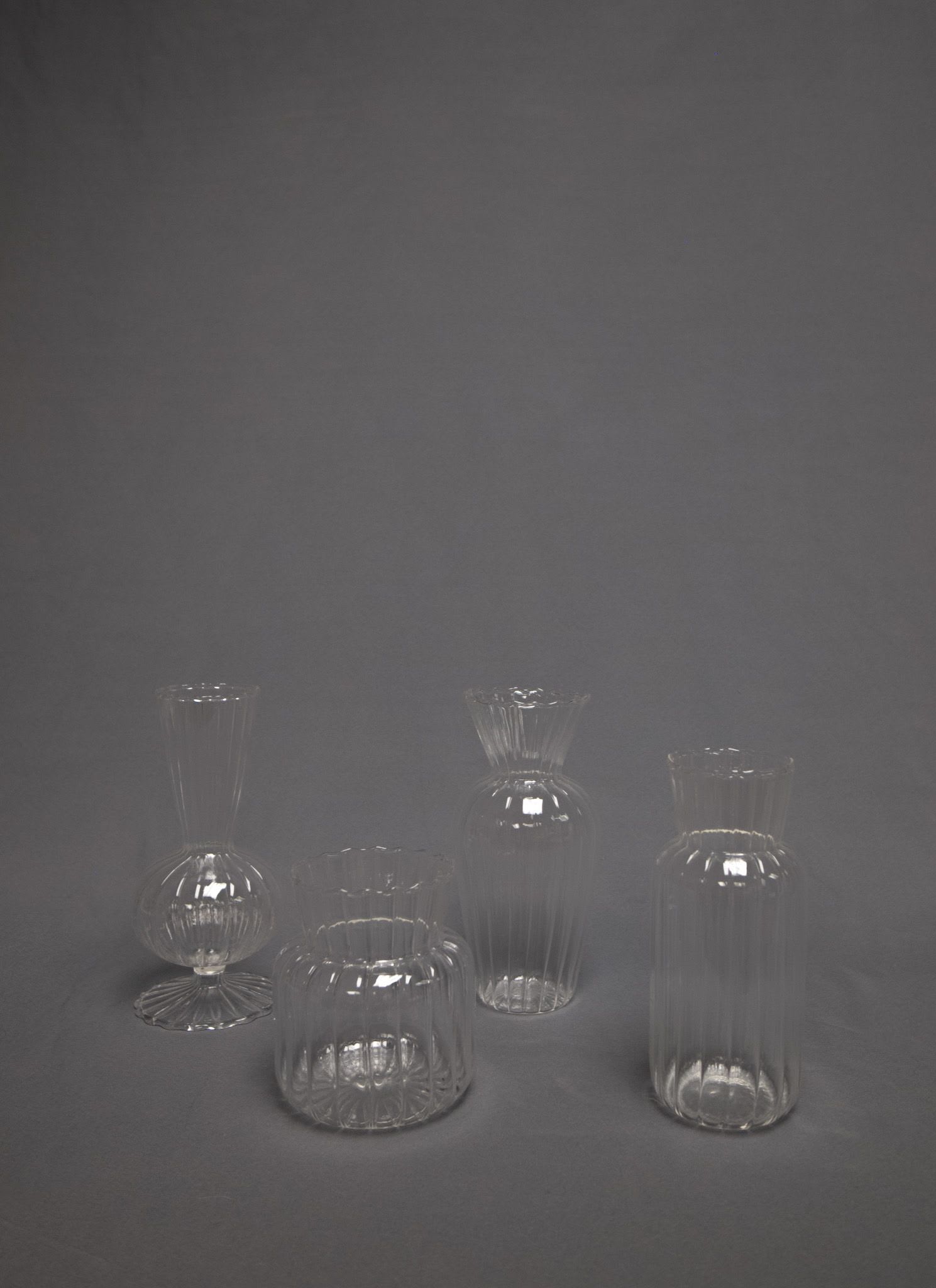 Set of four clear ribbed glass bud vases on a gray background