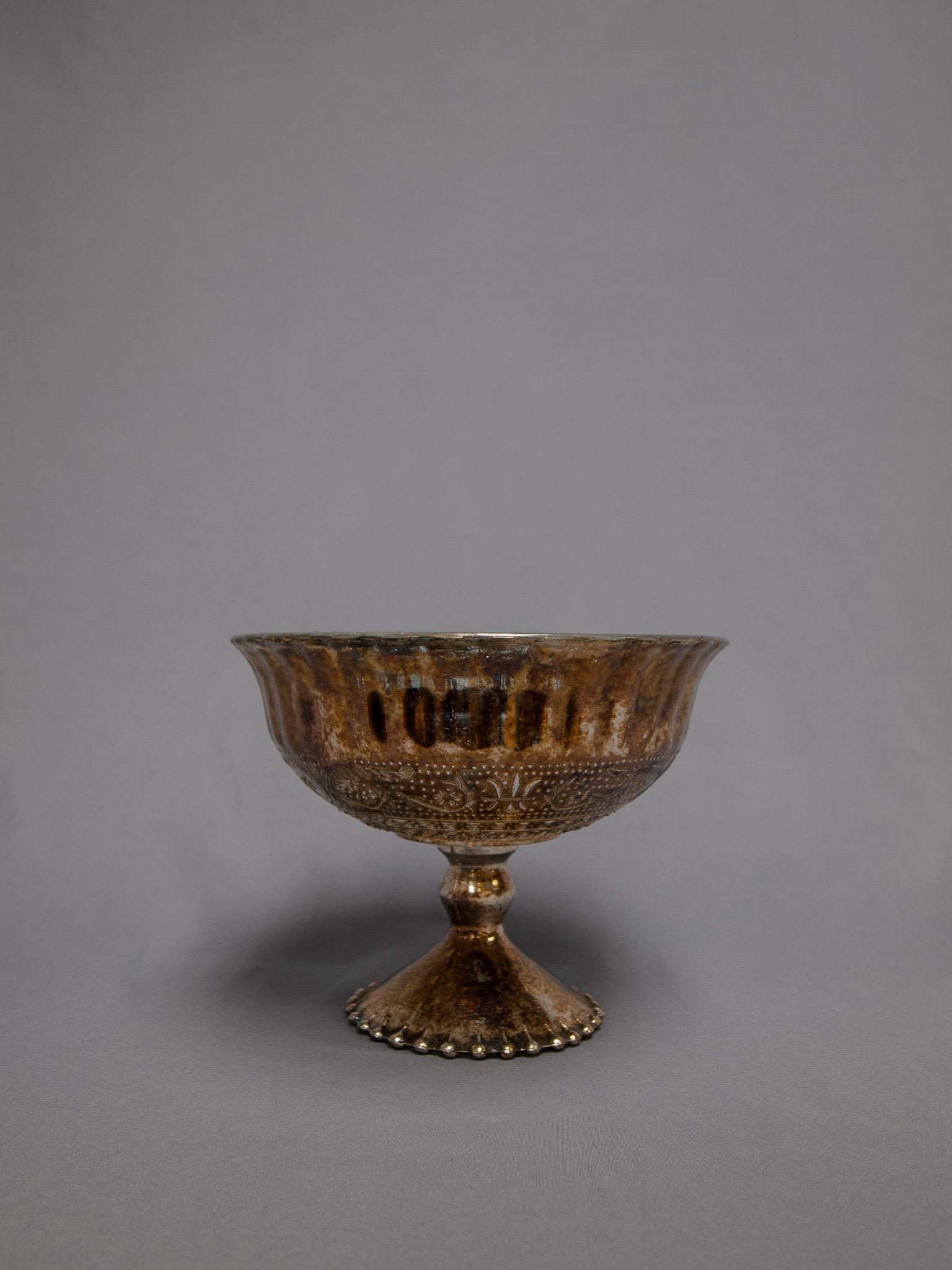 Bronze metallic pedestal compote bowl with decorative pattern on a gray background