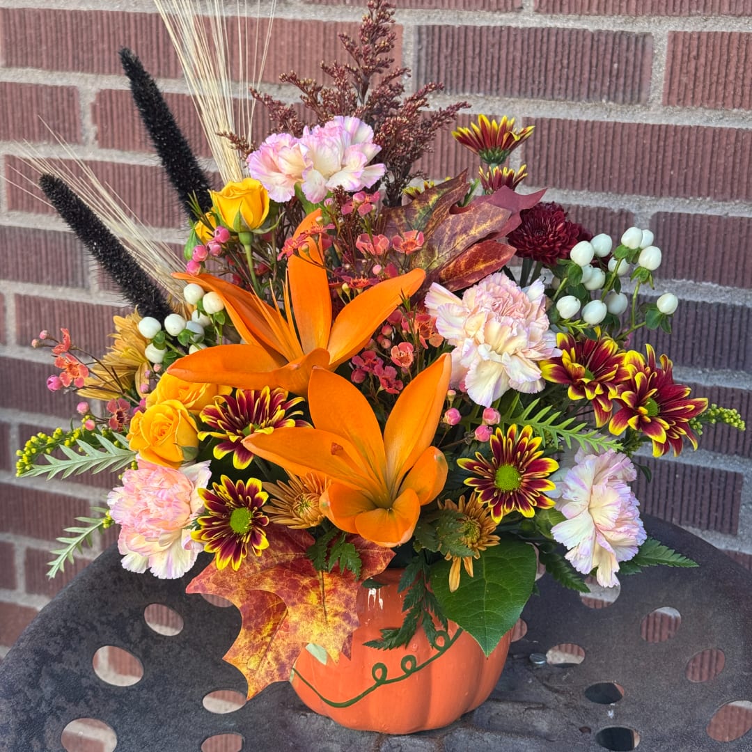 Autumn flower arrangement in an orange pumpkin container with lilies and mums