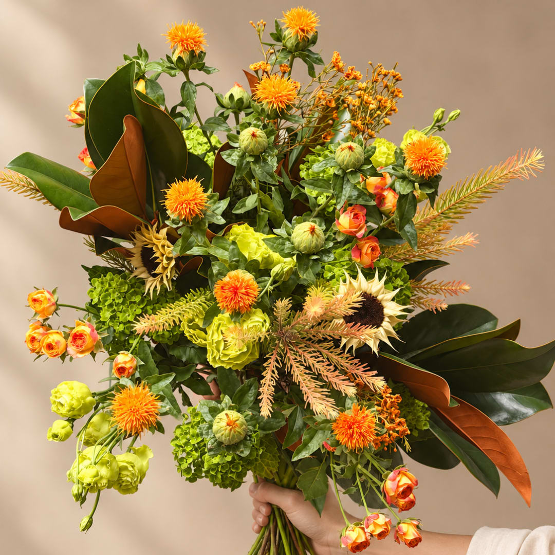 Handheld bouquet with orange blooms and green flowers in a loose, airy design