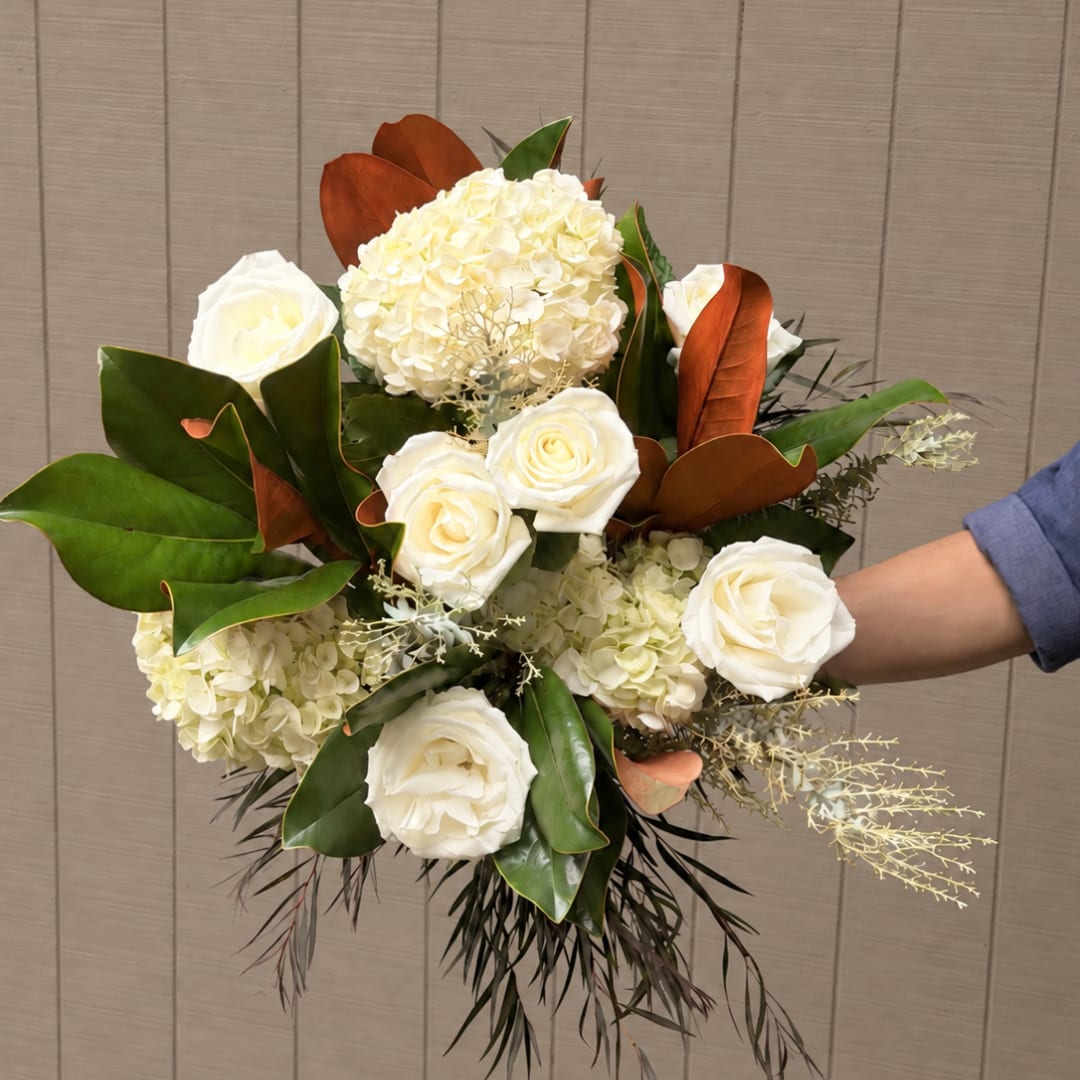 White roses and hydrangeas arranged with broad green and copper-toned foliage
