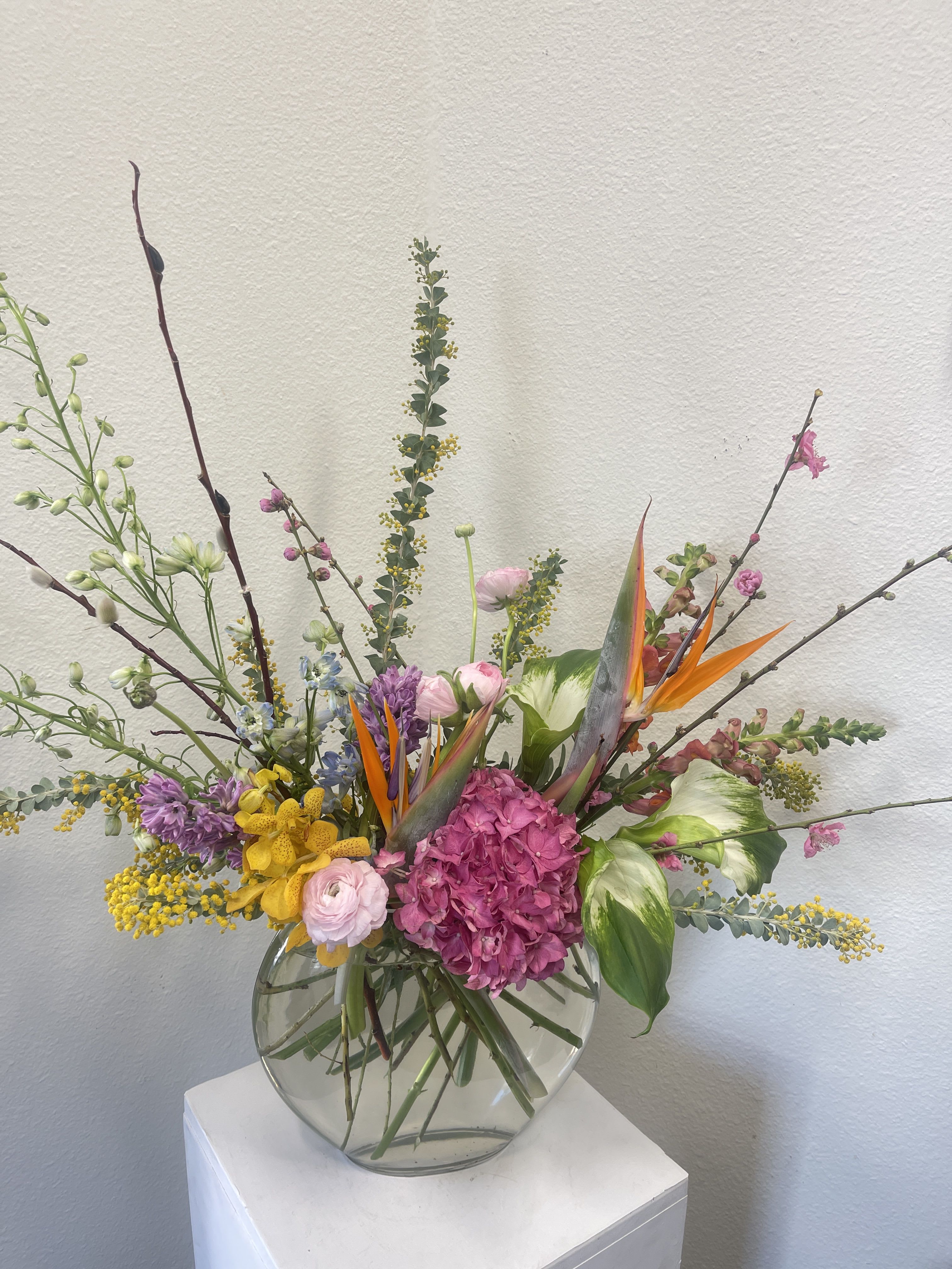 Mixed floral arrangement in a round glass vase with pink, yellow, purple, and orange blooms