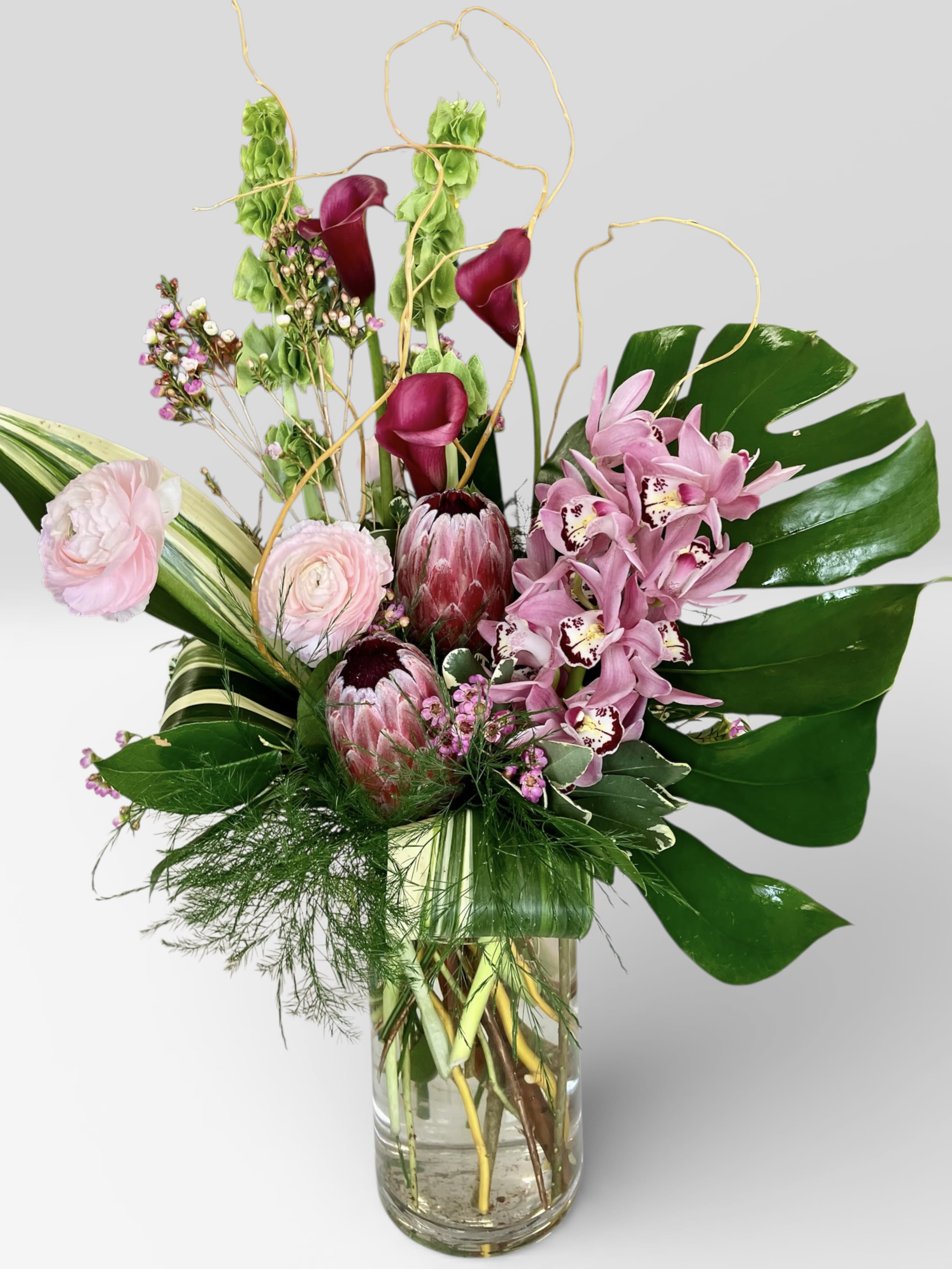 Pink orchids and calla lilies in a glass vase with tropical leaves