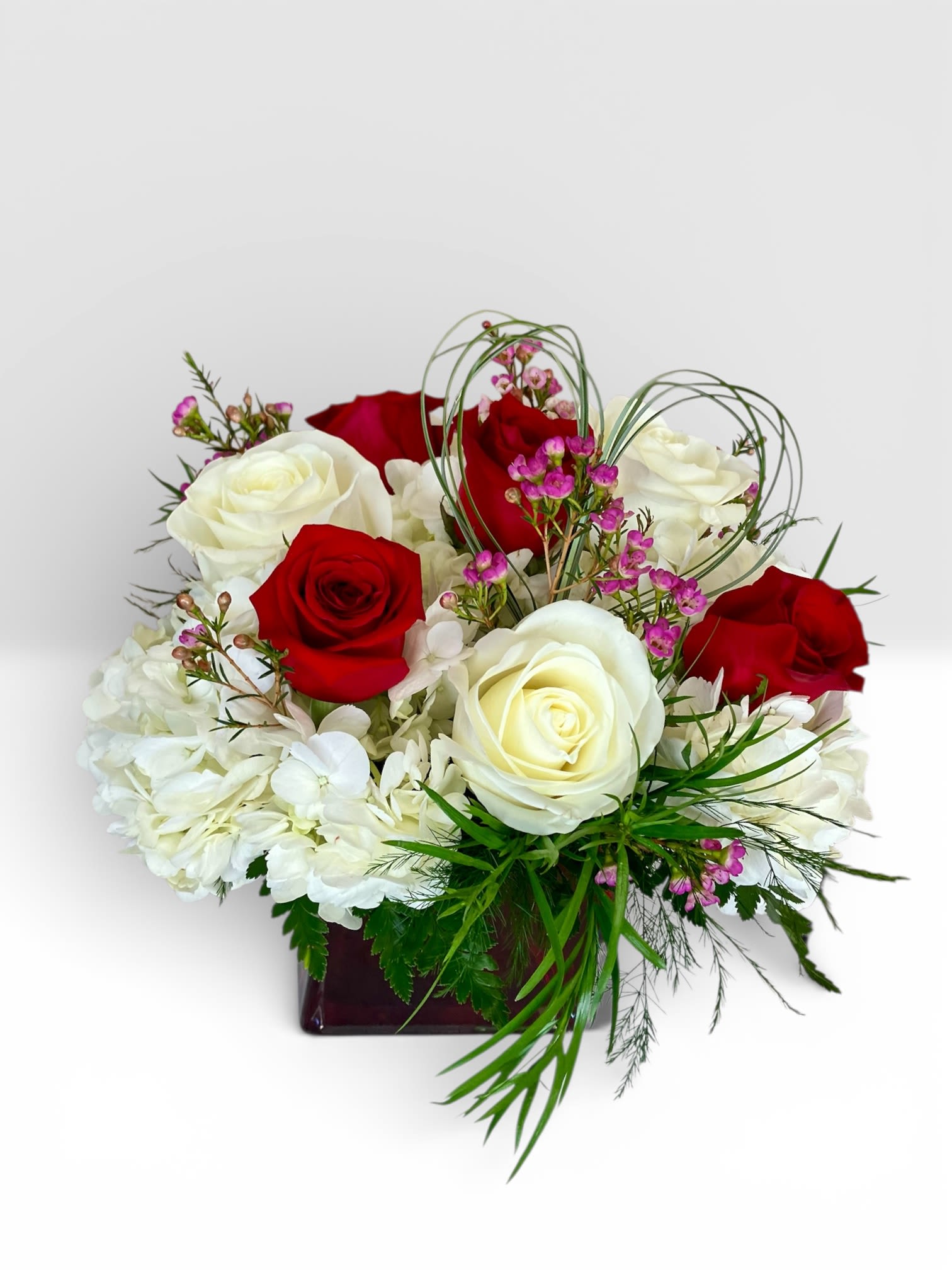 Red and white roses arranged in a square vase with small pink accents