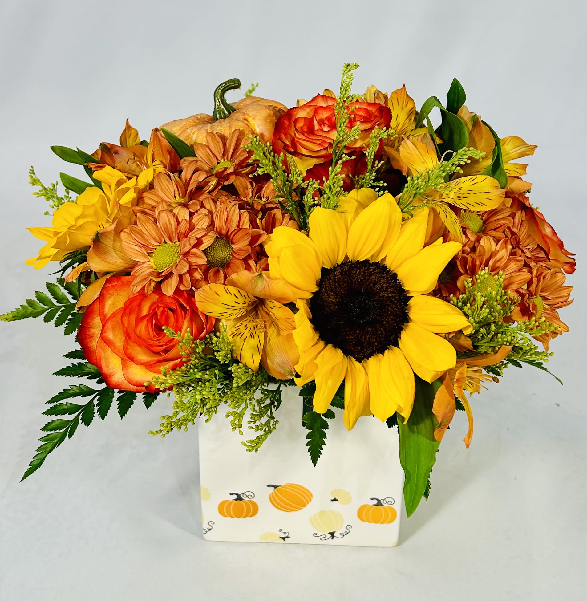 Autumn bouquet of sunflowers, roses, and mums in a pumpkin-decorated box