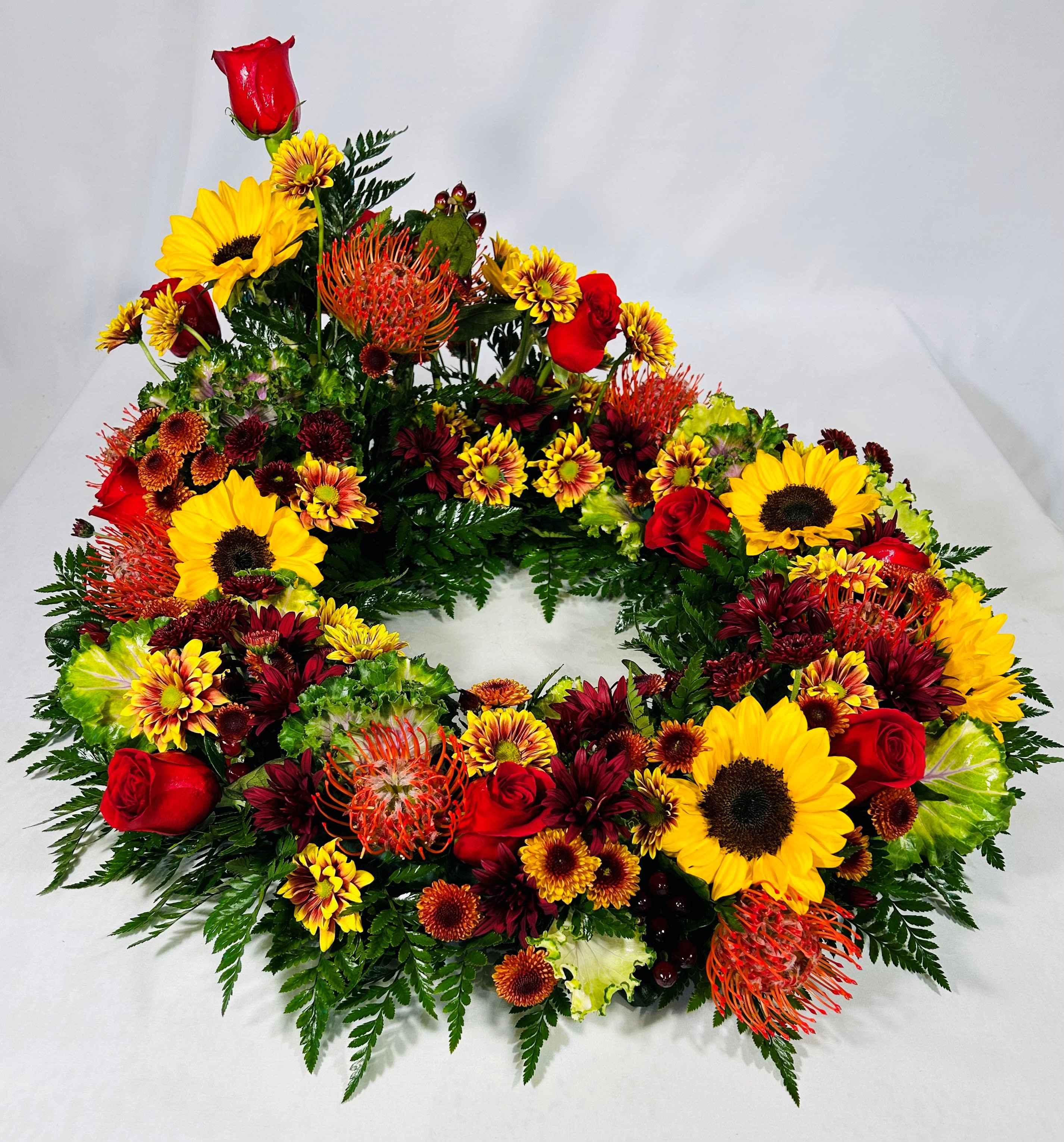 Circular floral wreath with sunflowers, red roses, and orange blooms