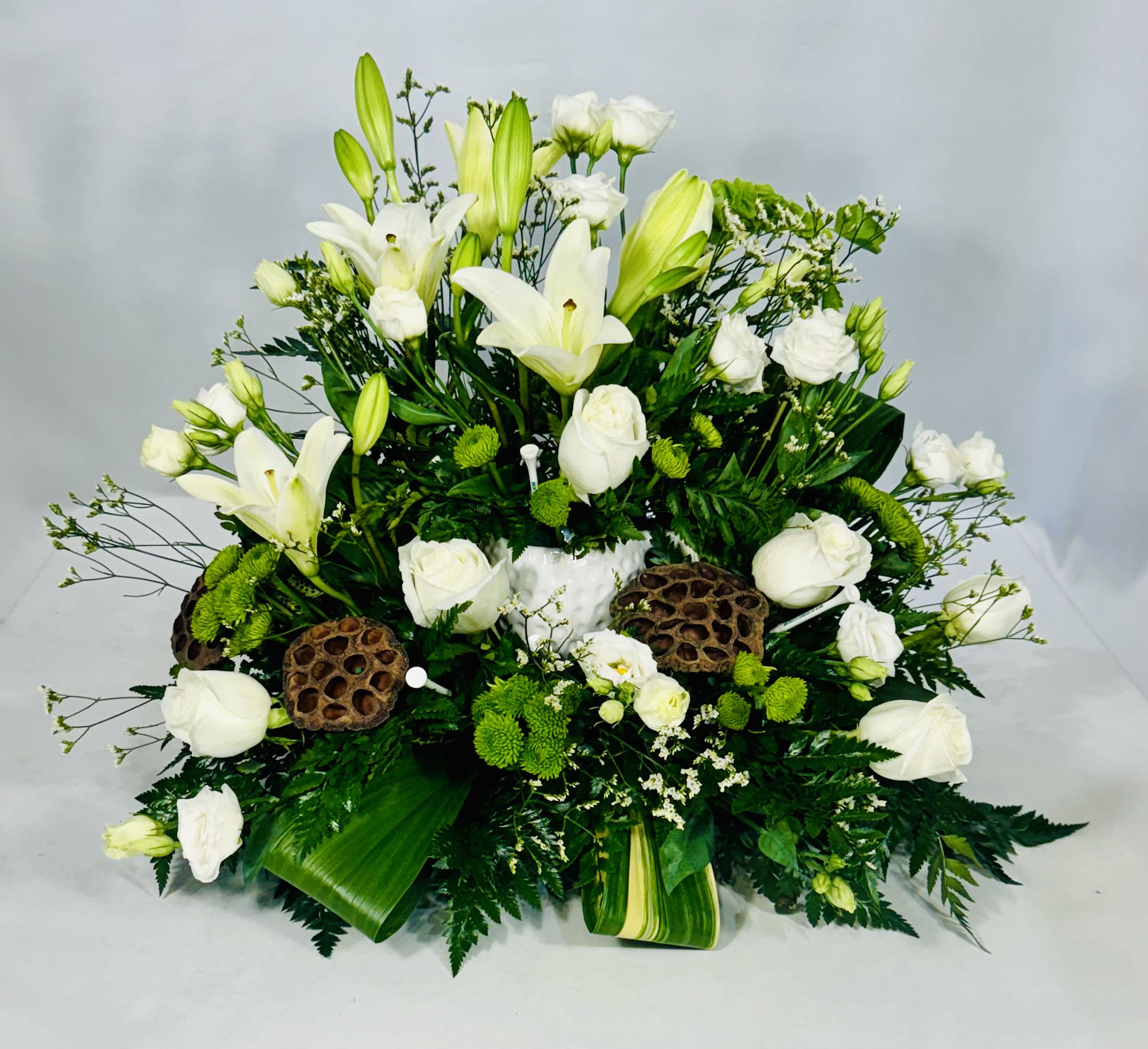 White lilies and roses arranged with green accents in a low centerpiece
