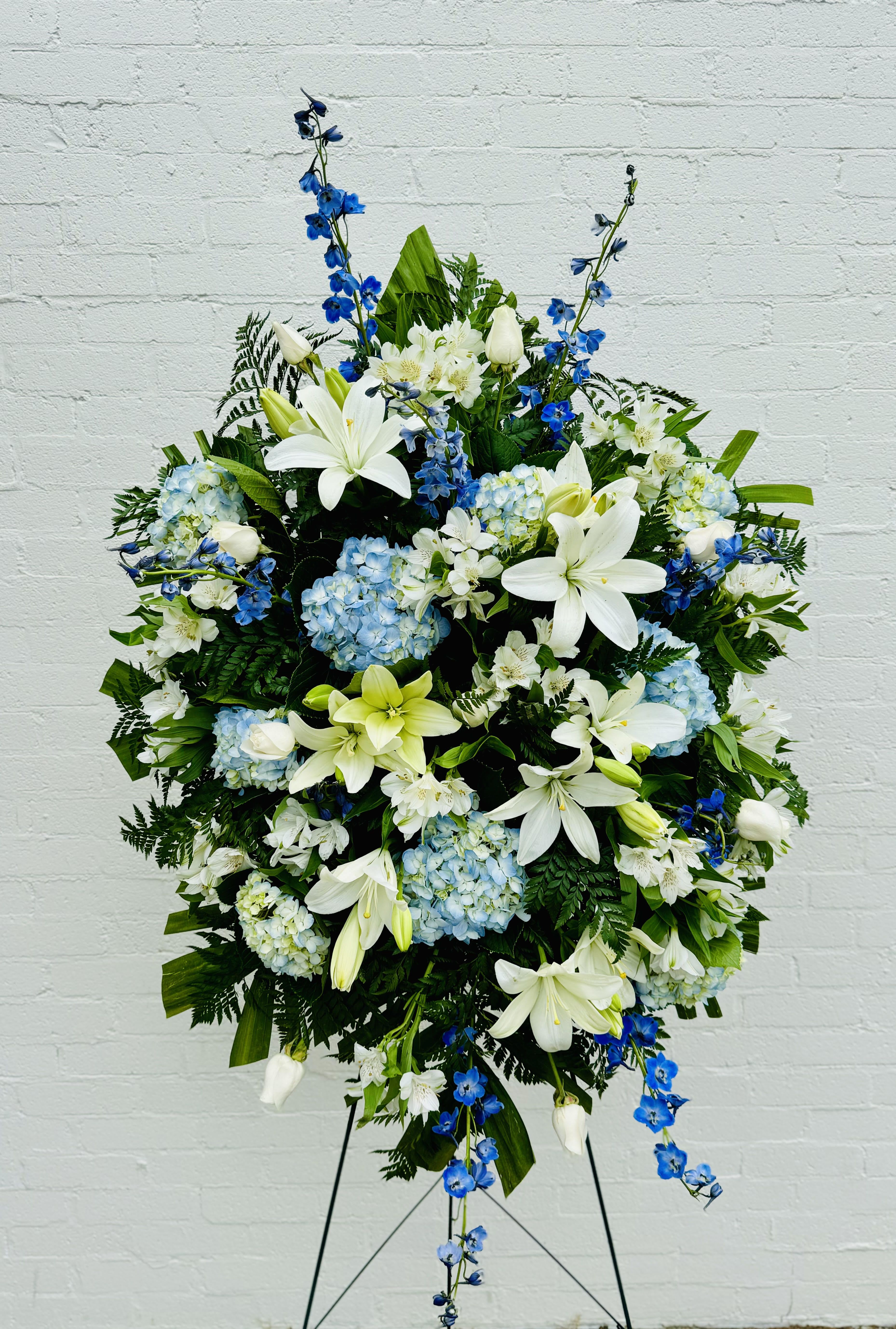 Large standing floral spray with white lilies, blue flowers, and hydrangeas