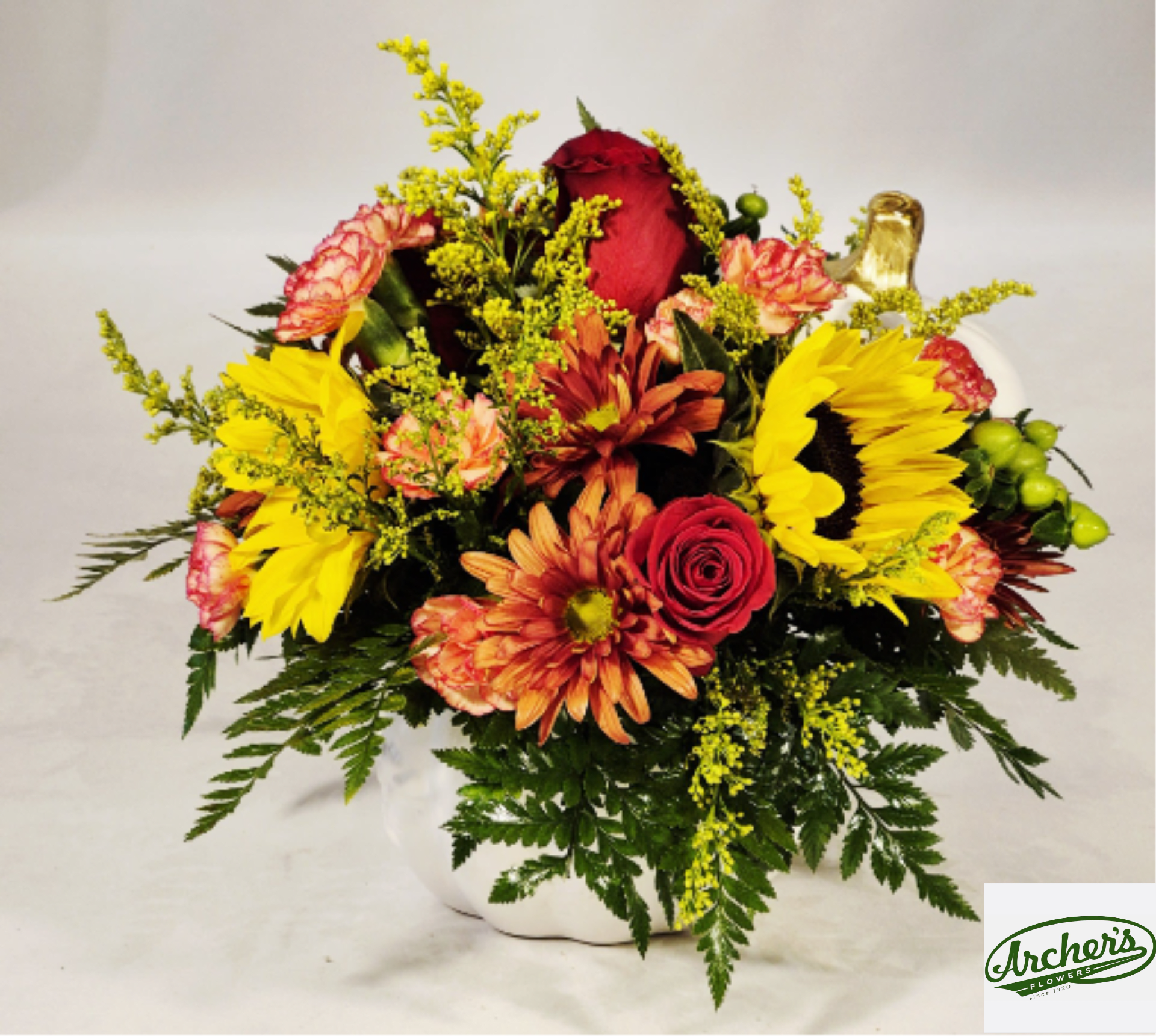Mixed bouquet with red roses, sunflowers, and orange mums in a white vase