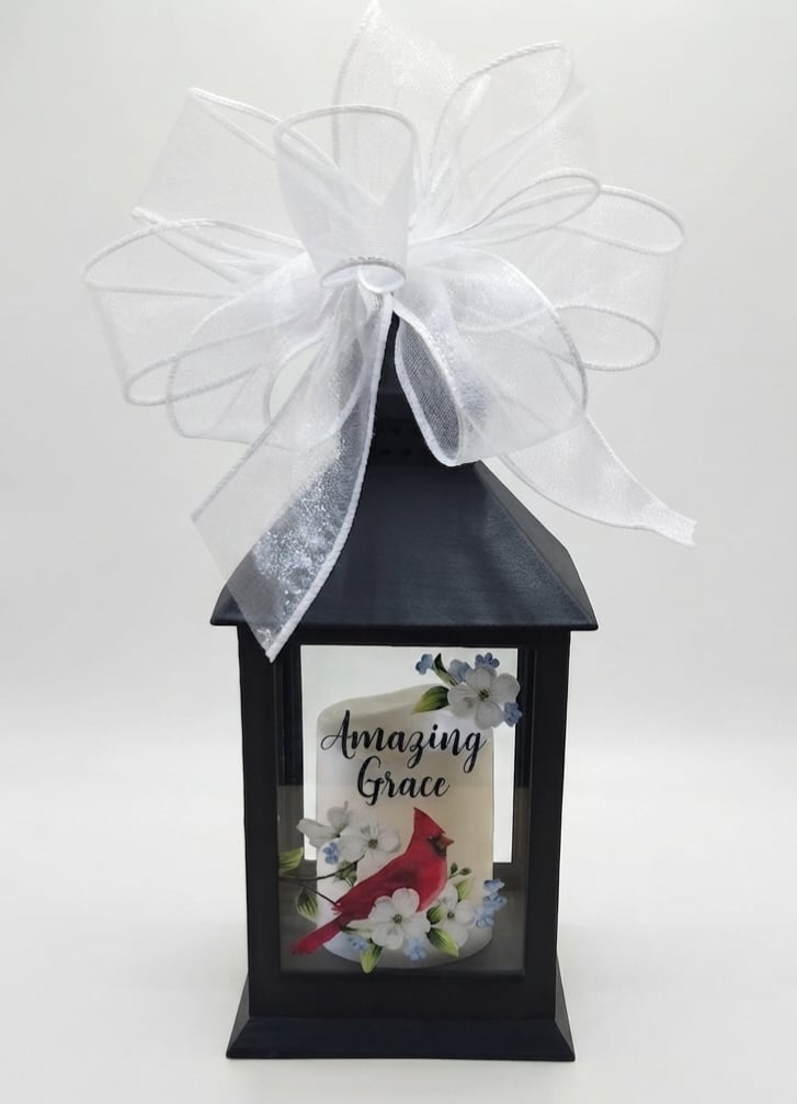Black lantern with a white bow and a candle labeled Amazing Grace