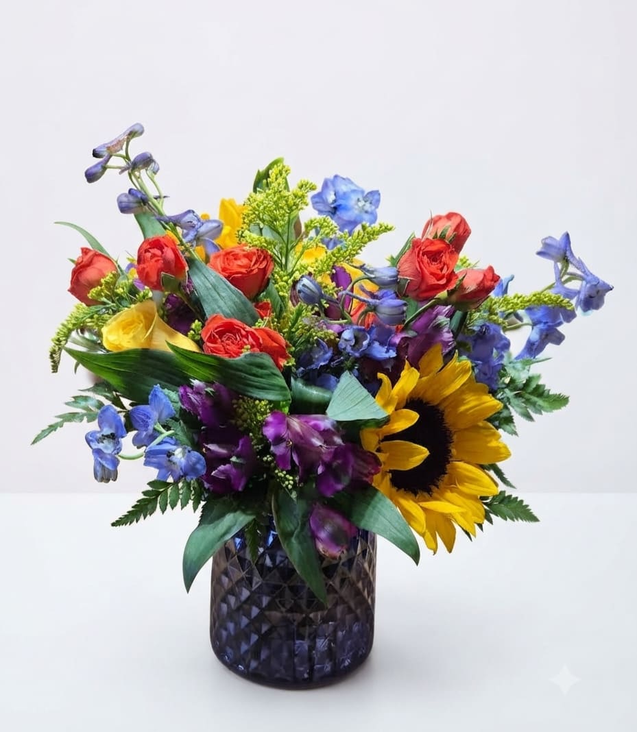 Colorful bouquet with roses, sunflowers, and blue flowers in a dark glass vase