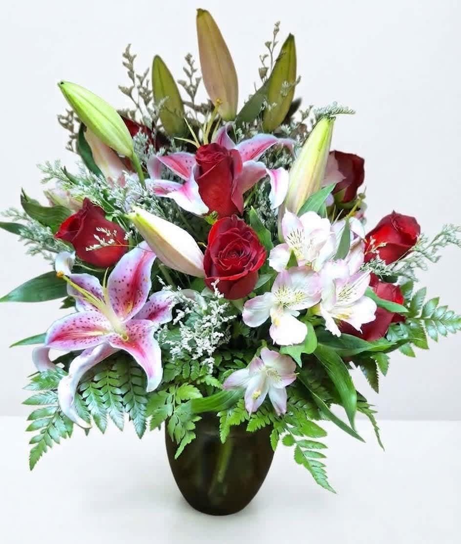 Bouquet of red roses and pink lilies in a dark glass vase