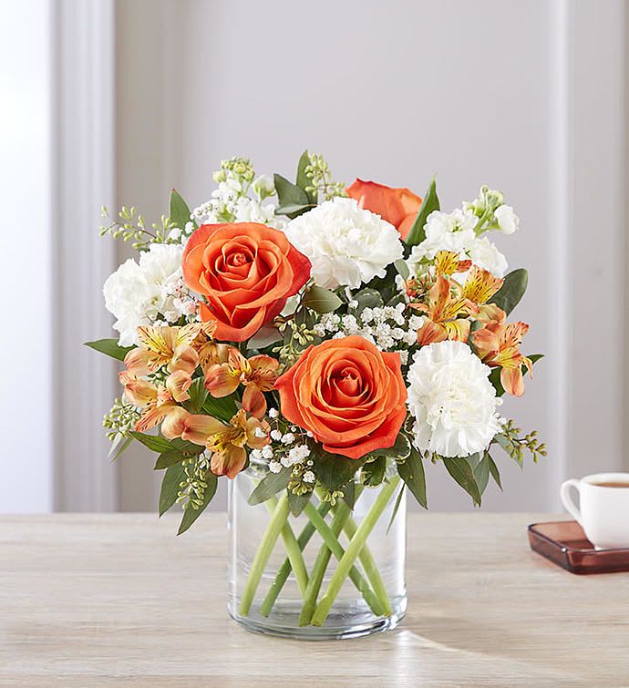 Orange roses and white carnations in a clear glass vase