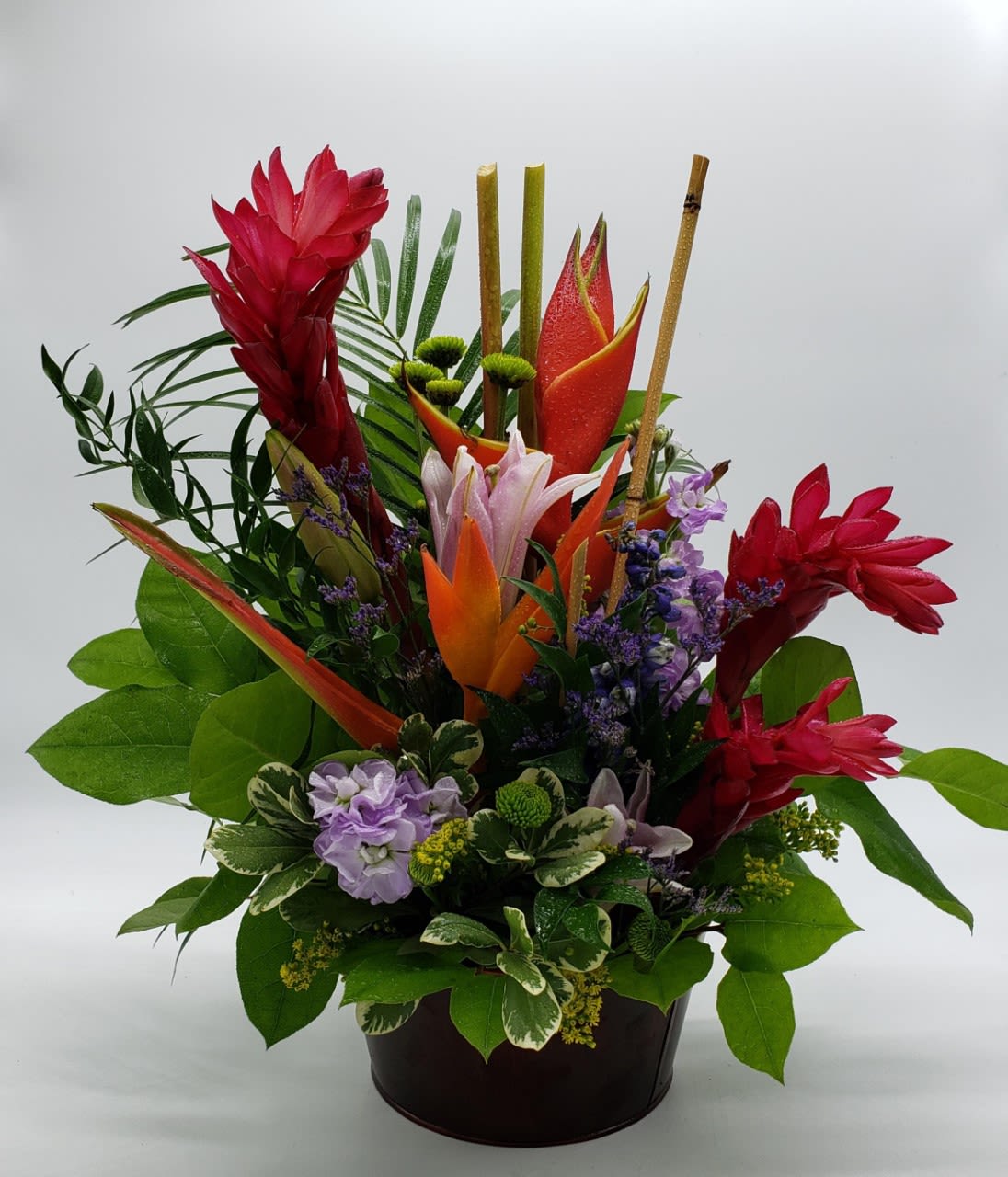 Tropical flower arrangement in a dark container with red and orange blooms