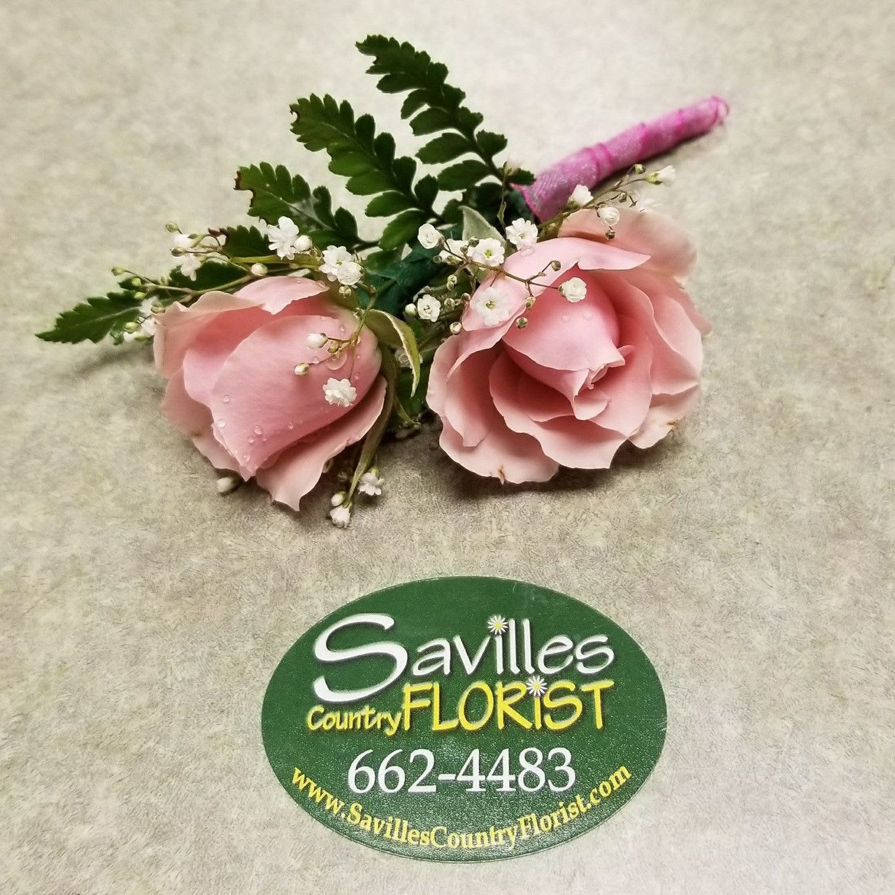 Two pink rose boutonnieres with baby's breath and greenery