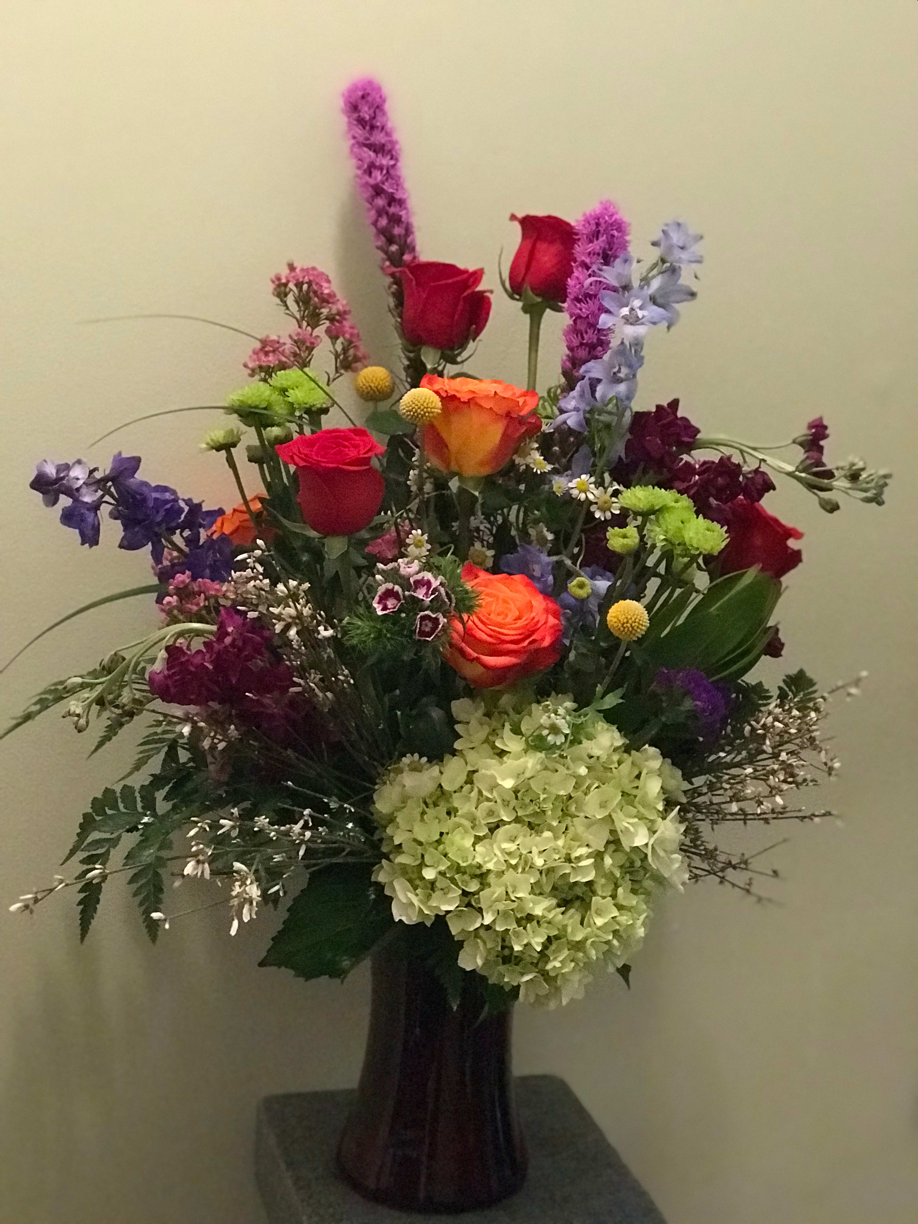 Tall mixed bouquet with roses, hydrangea, and purple accent flowers in a dark vase