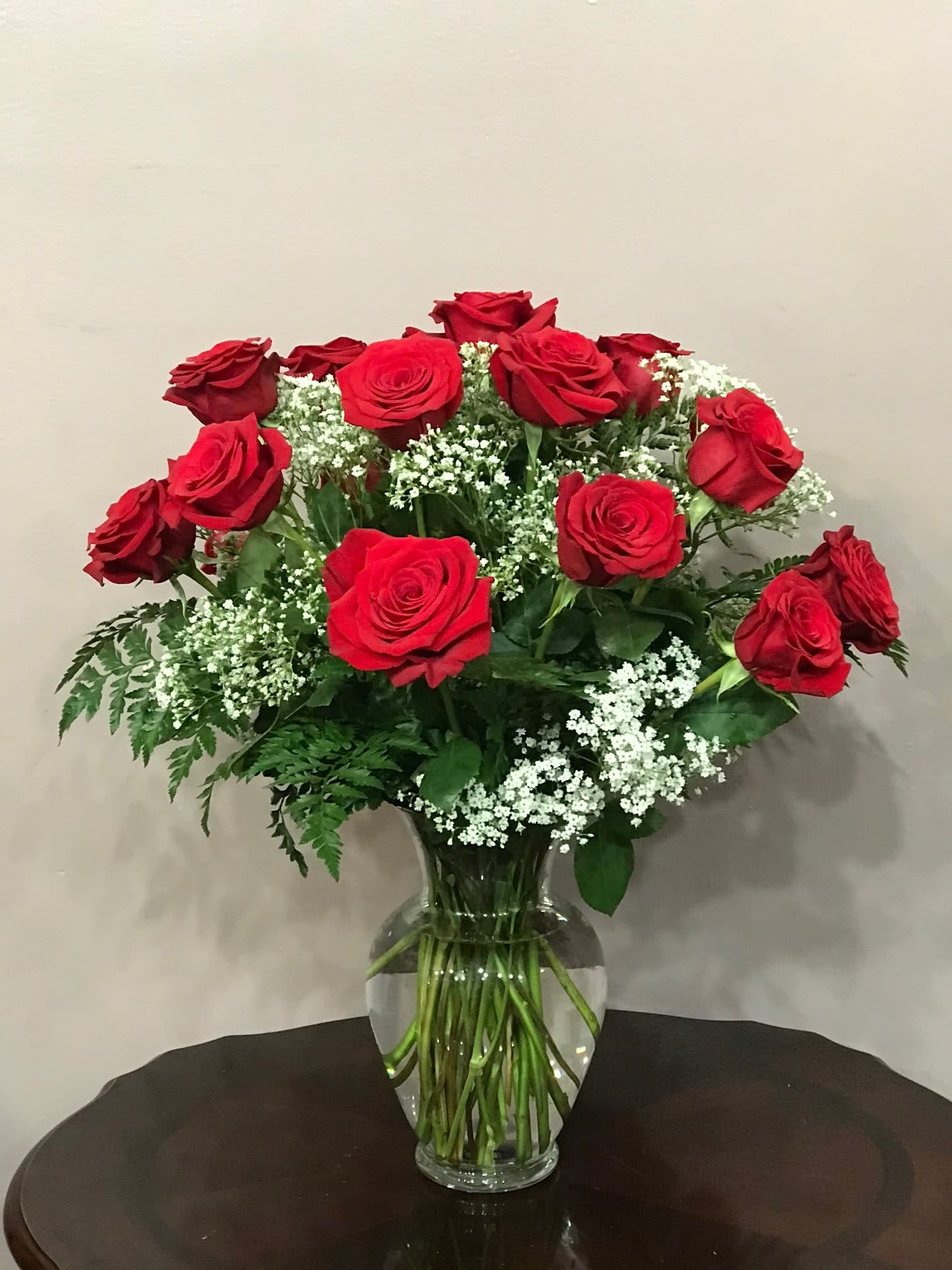 Red roses arranged in a clear glass vase with white filler flowers