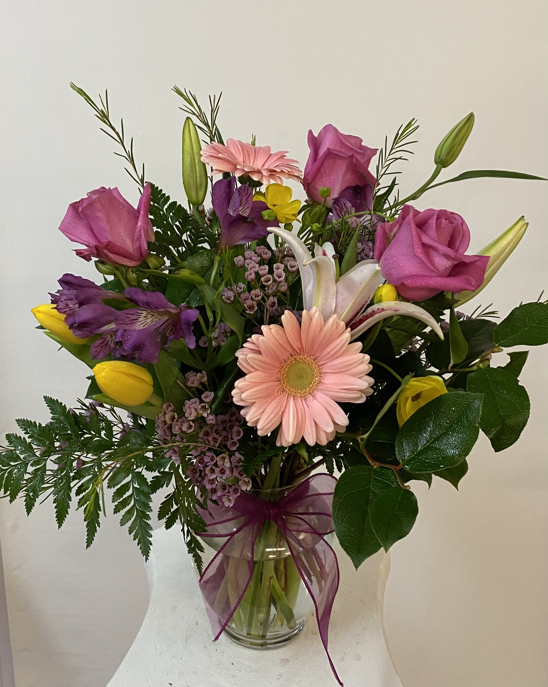 Mixed bouquet with pink roses, lilies, tulips, and a gerbera daisy in a glass vase