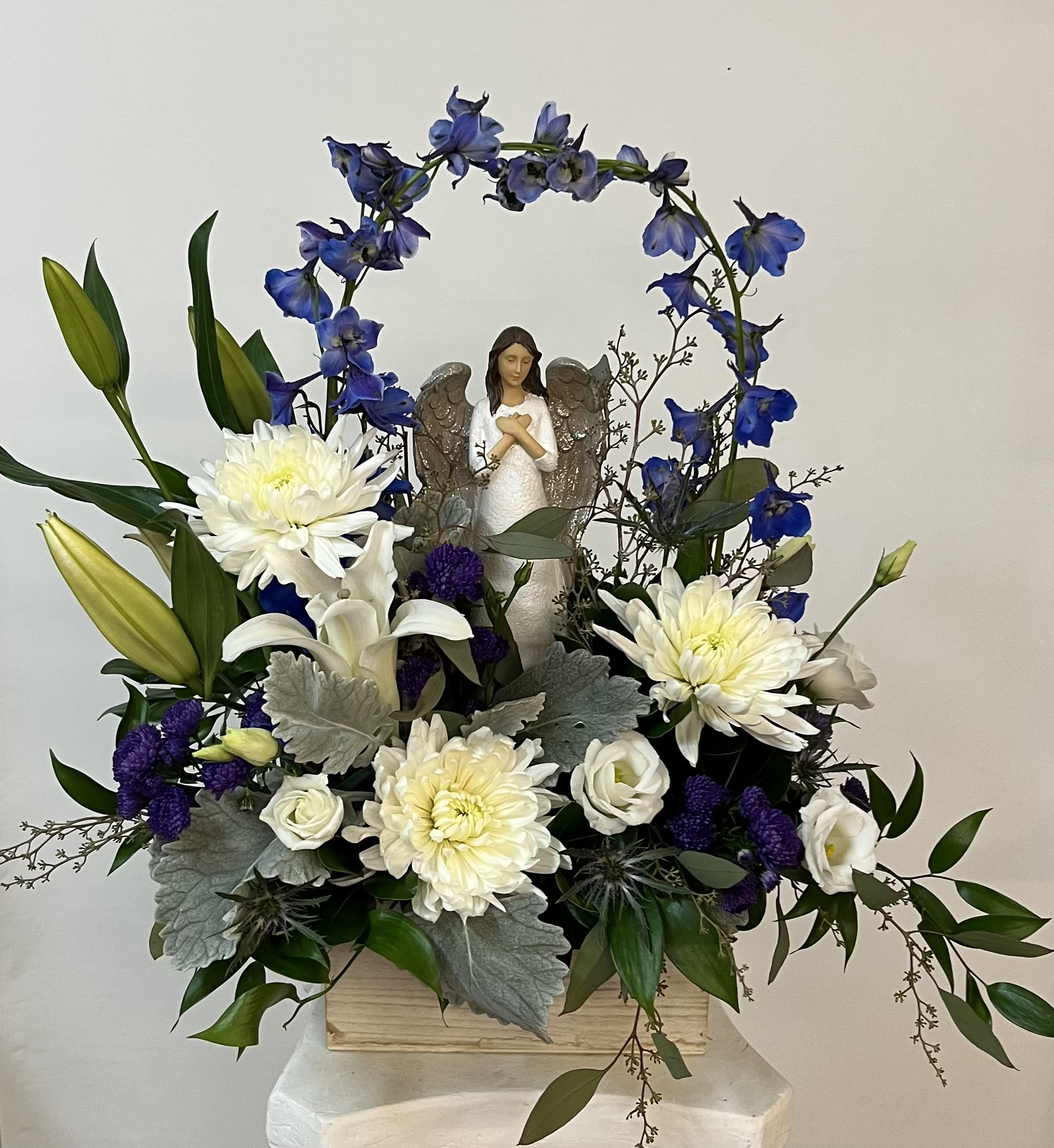 White and blue floral arrangement with an angel figurine in a wooden box