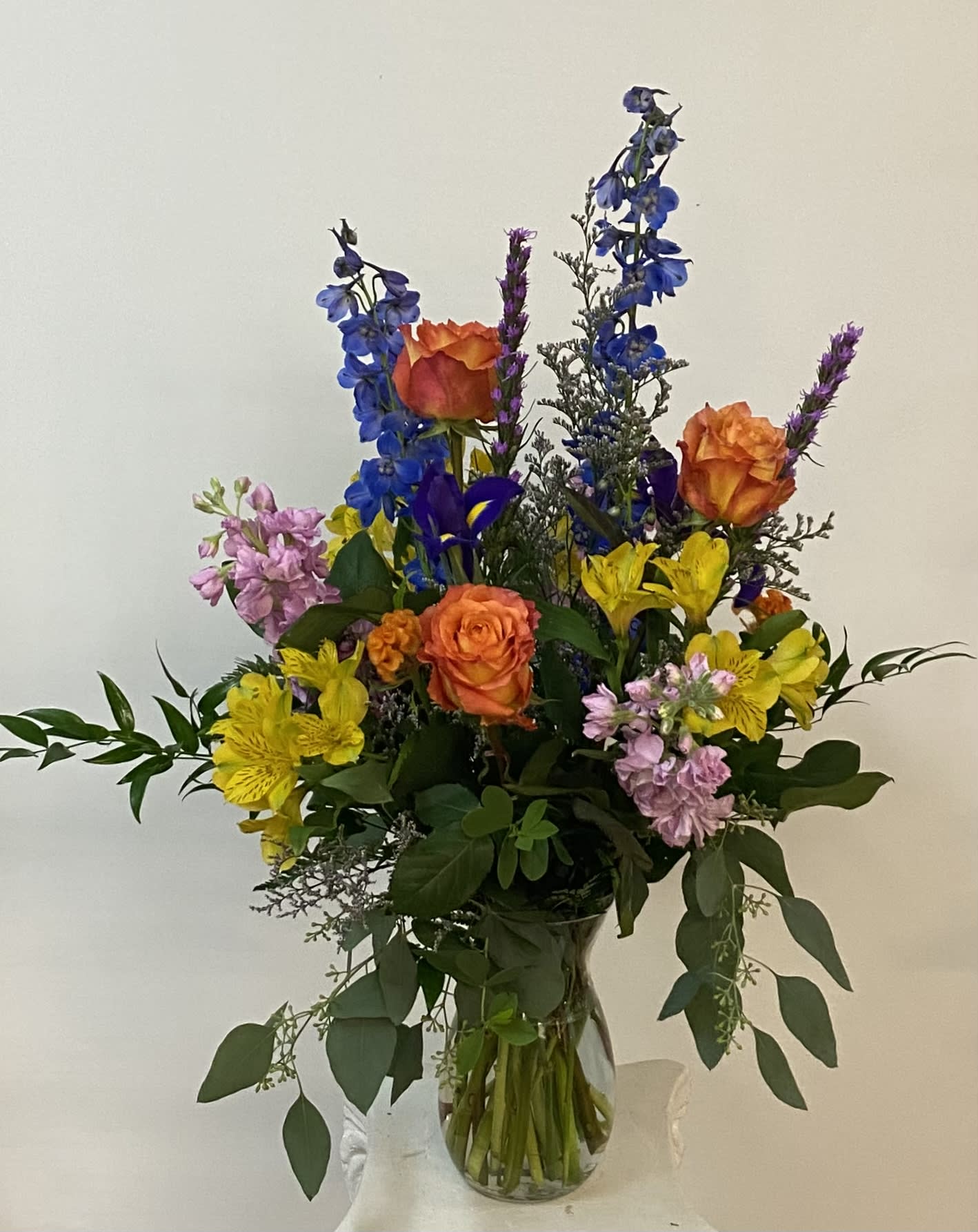 Mixed bouquet of orange roses, blue delphinium, and yellow alstroemeria in a glass vase