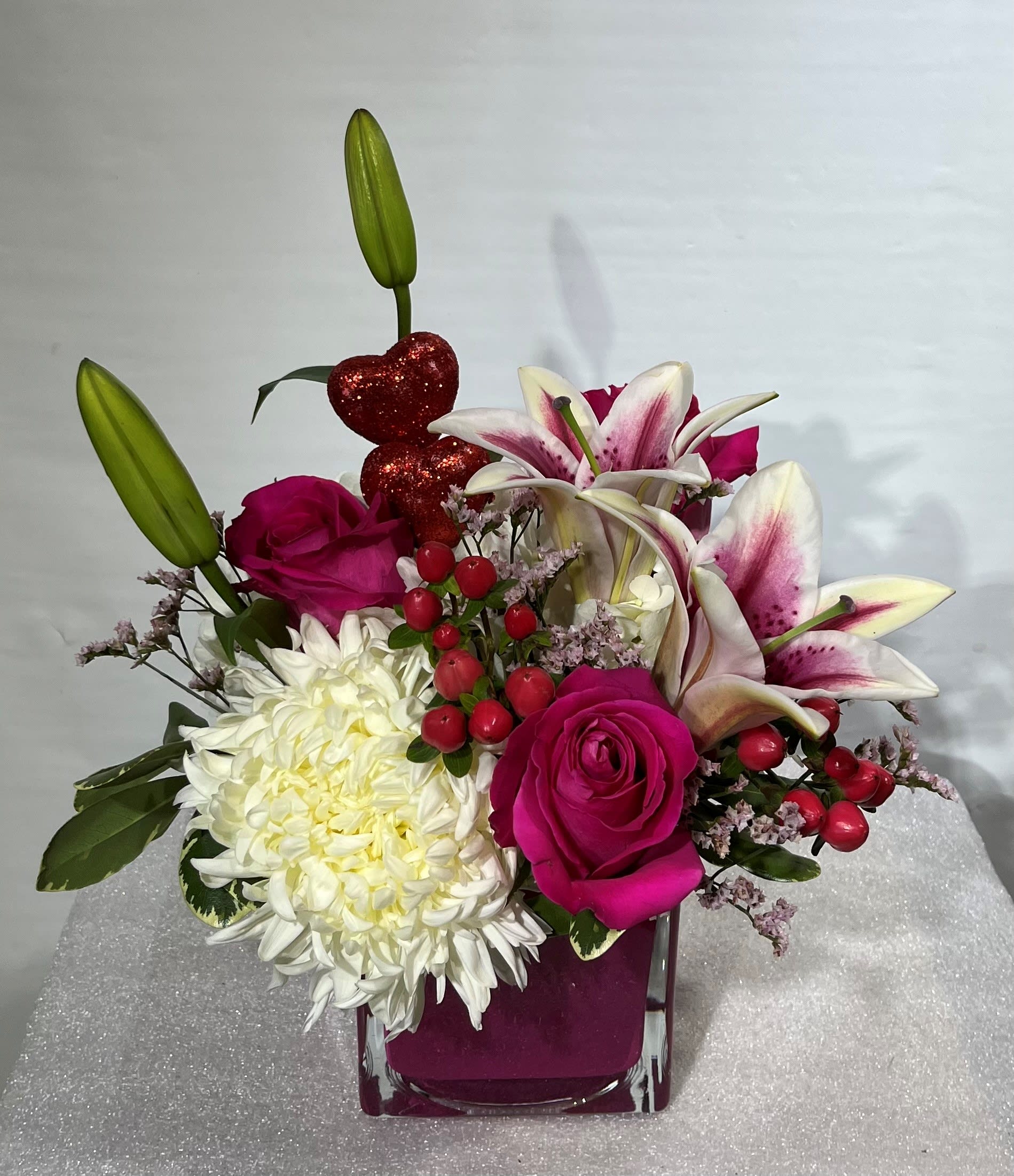 Pink roses and white lilies in a square glass vase with a white chrysanthemum