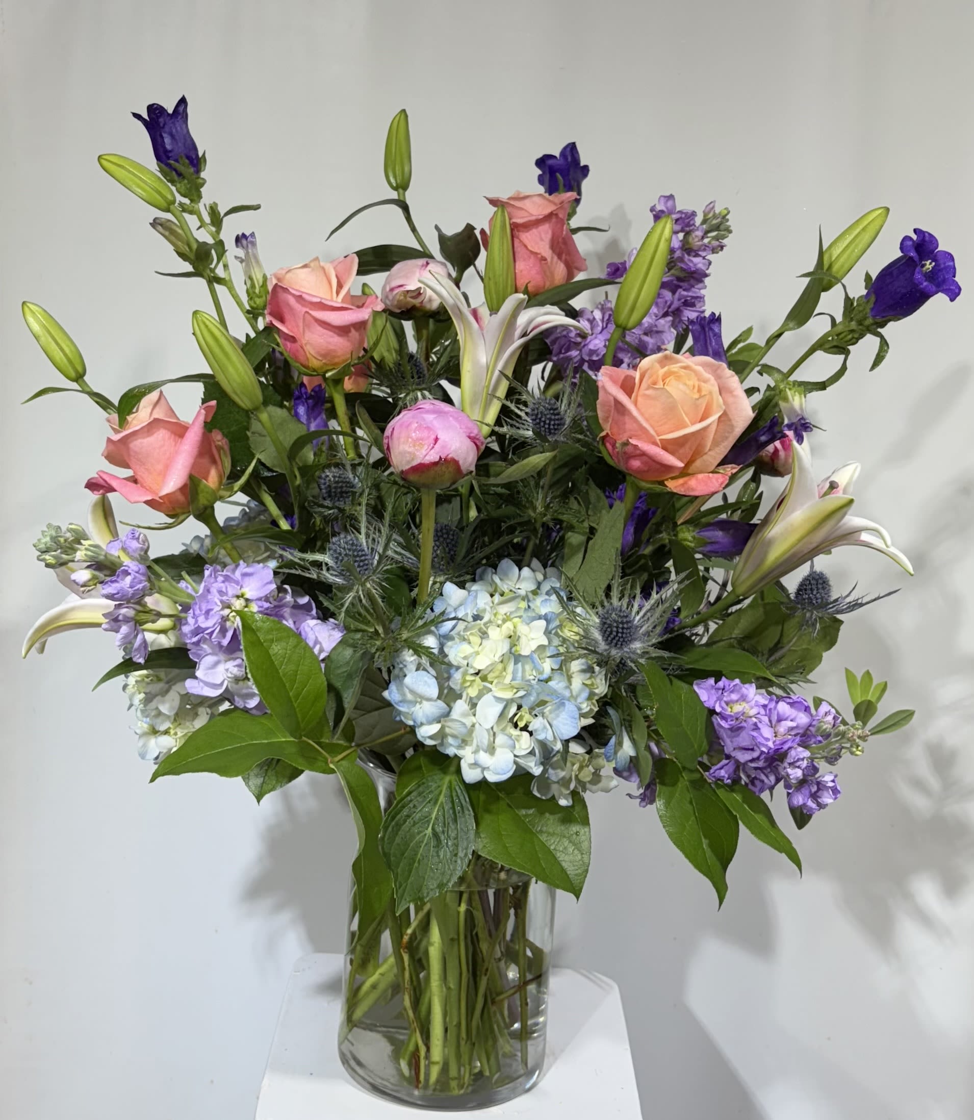 Mixed bouquet of pink roses, lilies, and purple flowers in a glass vase