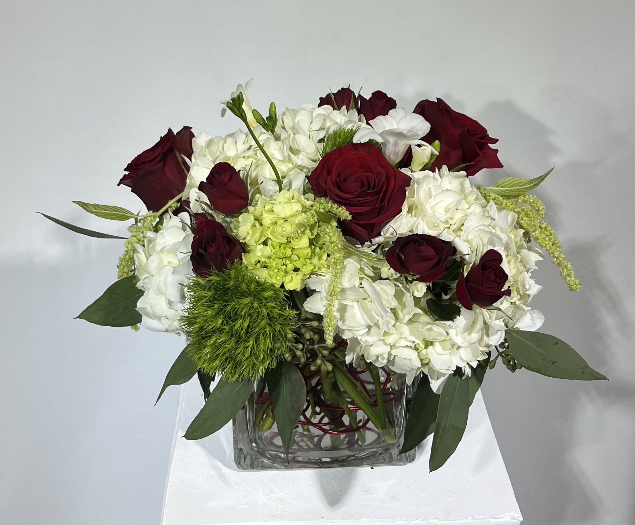 Red roses and white hydrangeas in a clear square vase