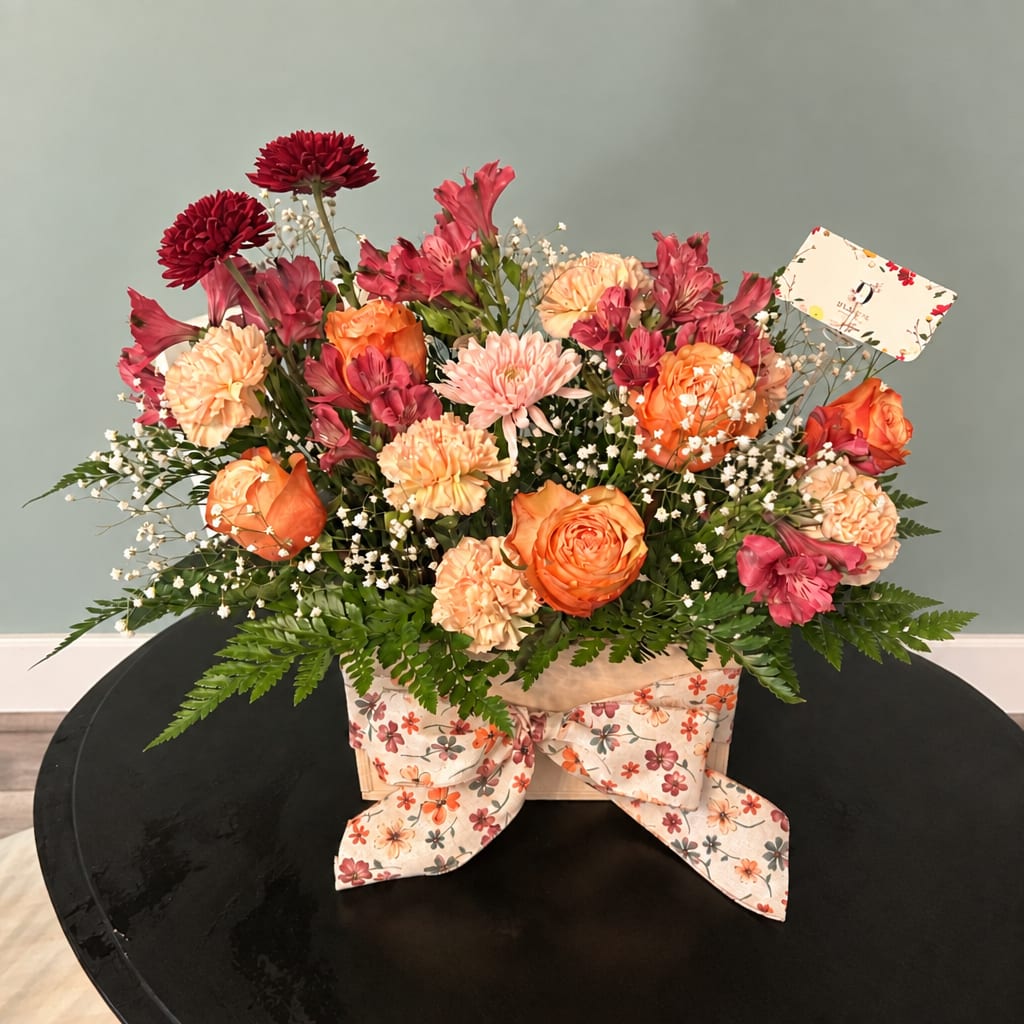 Mixed bouquet of orange and pink flowers in a floral box with a ribbon