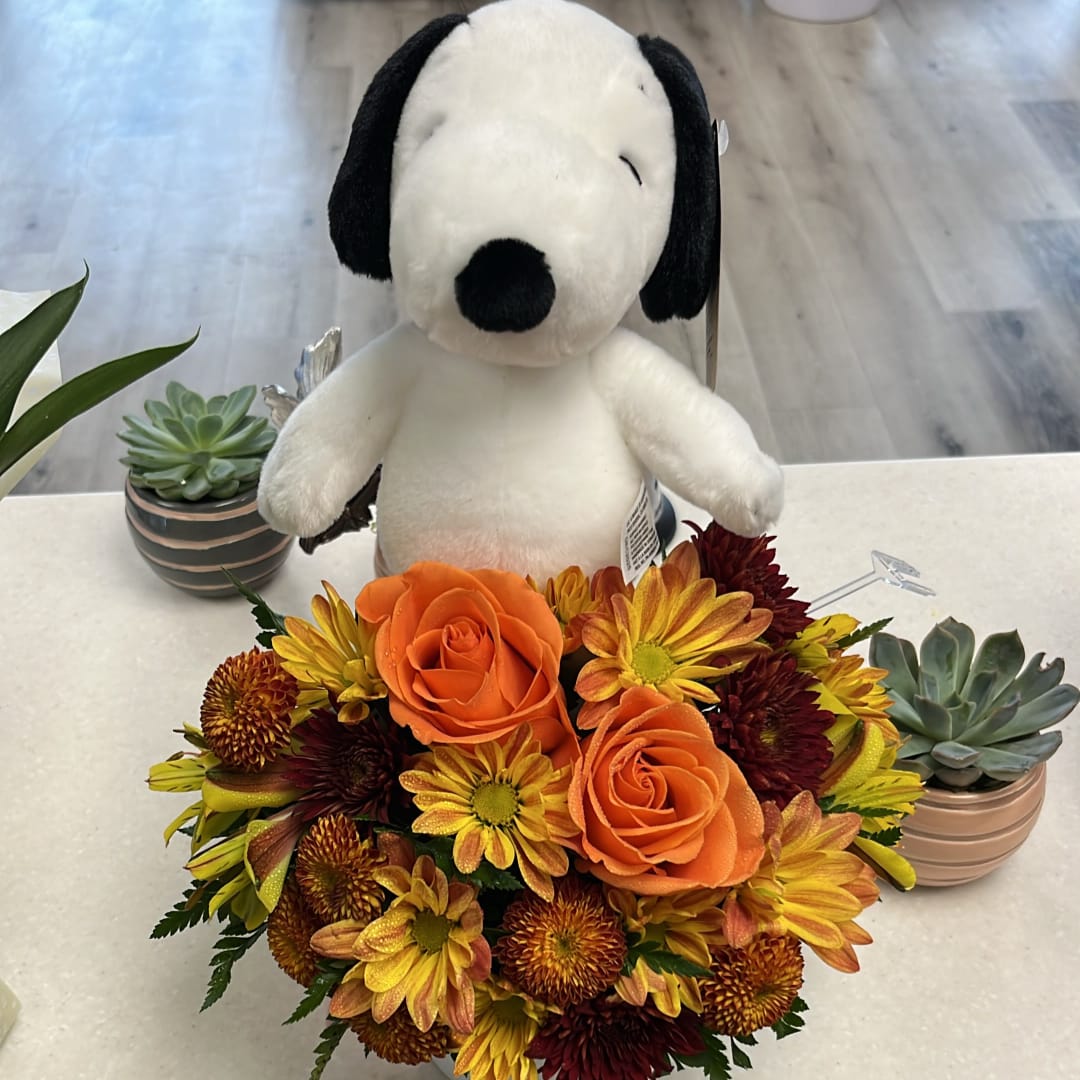 Orange roses and yellow chrysanthemums in a low arrangement with a plush Snoopy toy behind it