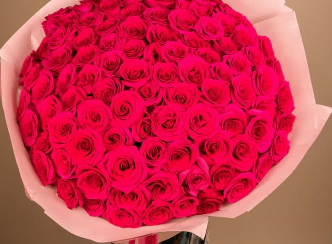 Large bouquet of bright pink roses wrapped in pale paper