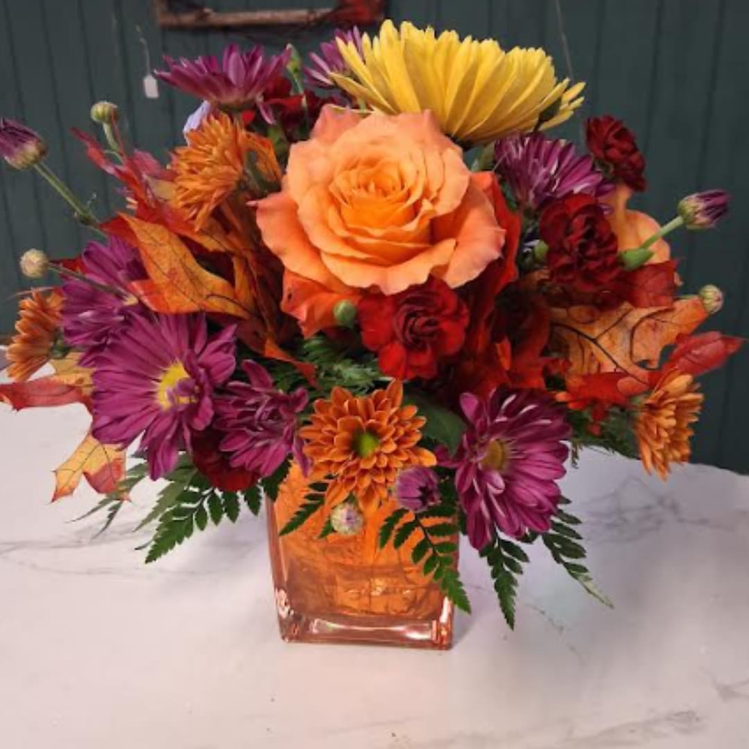 Orange and purple floral arrangement in a square glass vase