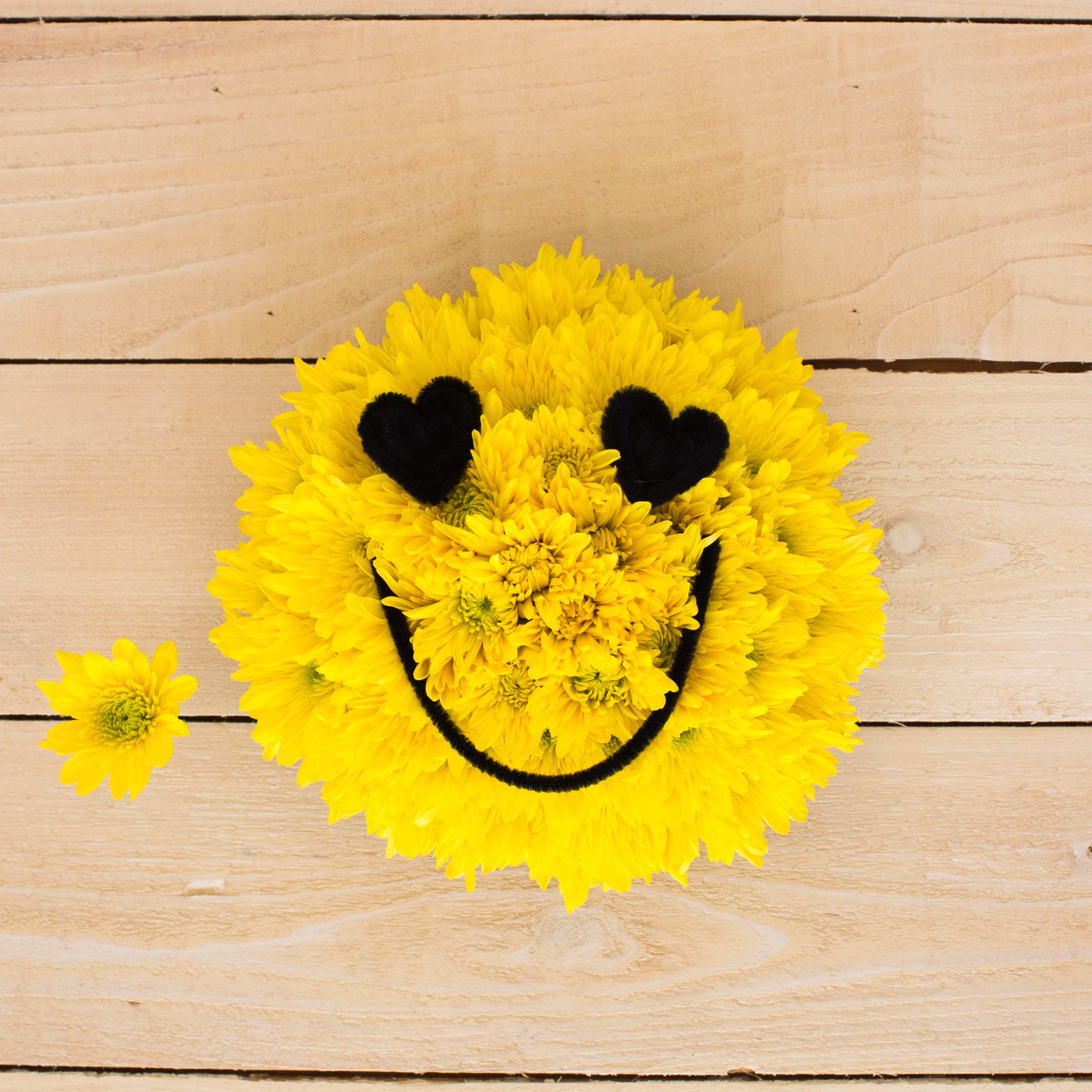 Round yellow daisy arrangement shaped like a smiley face with black heart eyes on wood surface