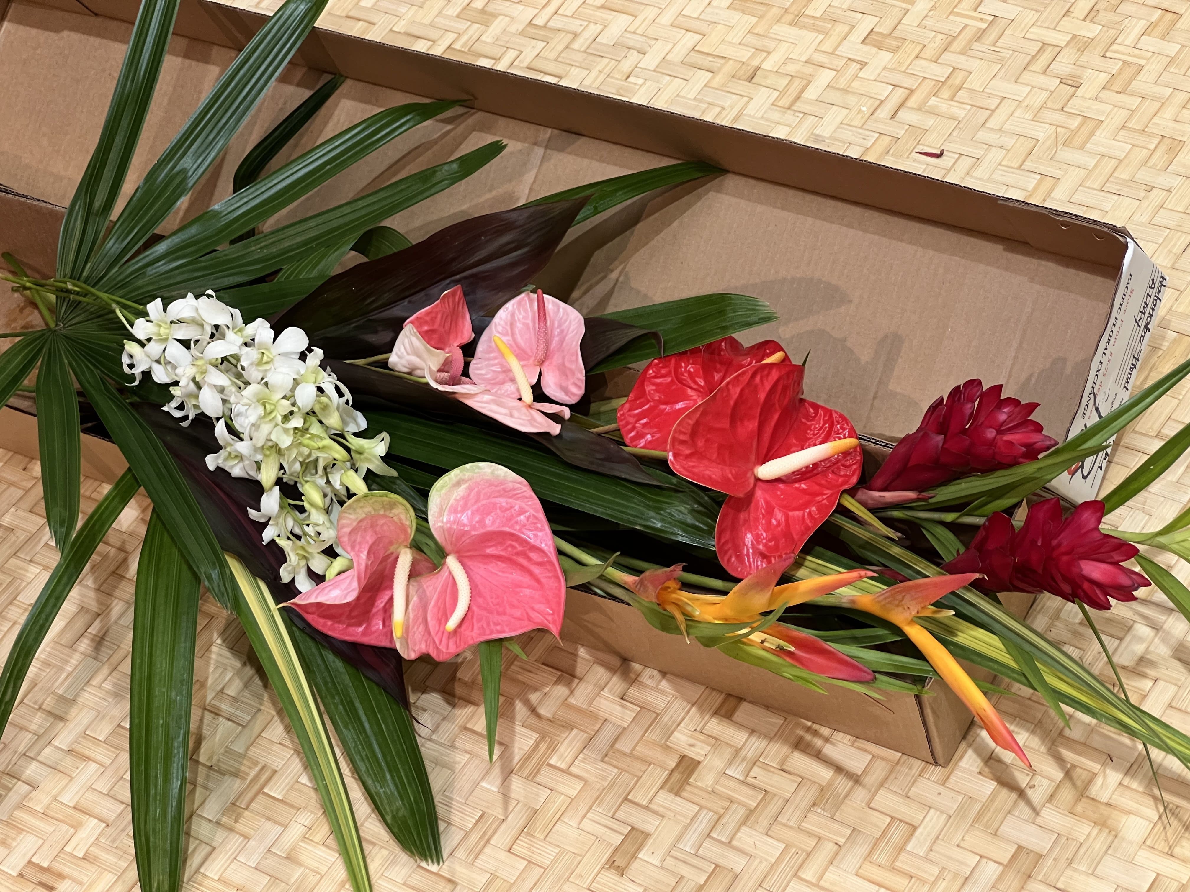 Assorted tropical cut flowers in bright colors arranged loosely in an open cardboard box