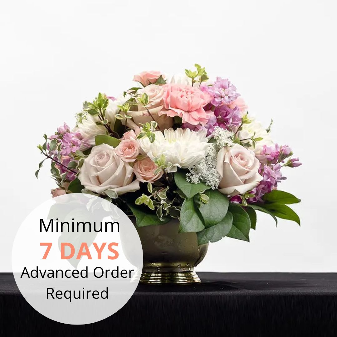 Low pastel arrangement of roses, carnations, and mums in a gold urn with a 7-day advance order text overlay.
