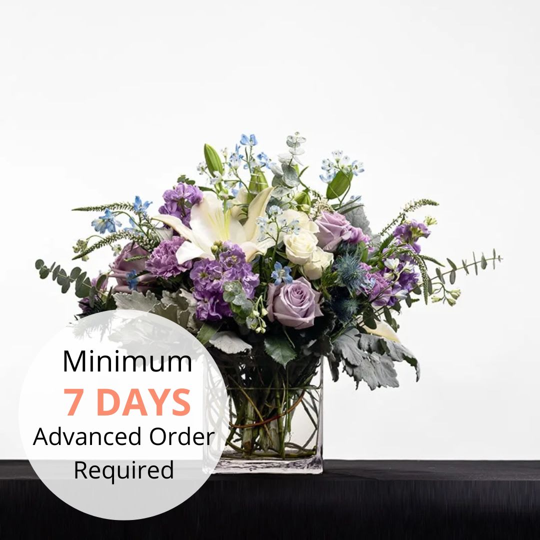 Rectangular glass vase with white lilies, lavender roses, and purple flowers in a lush arrangement