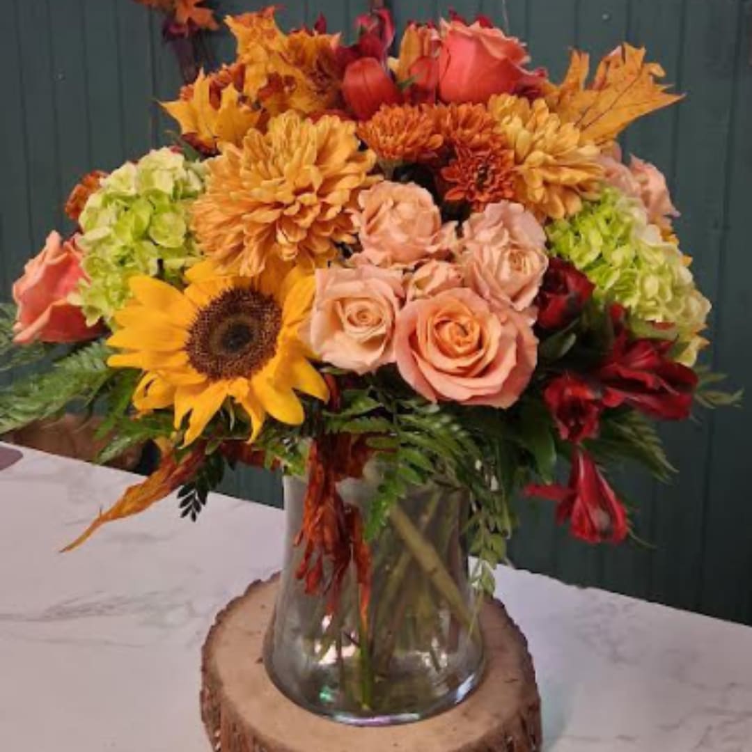 Autumn bouquet of sunflowers, roses, and mums in a glass vase
