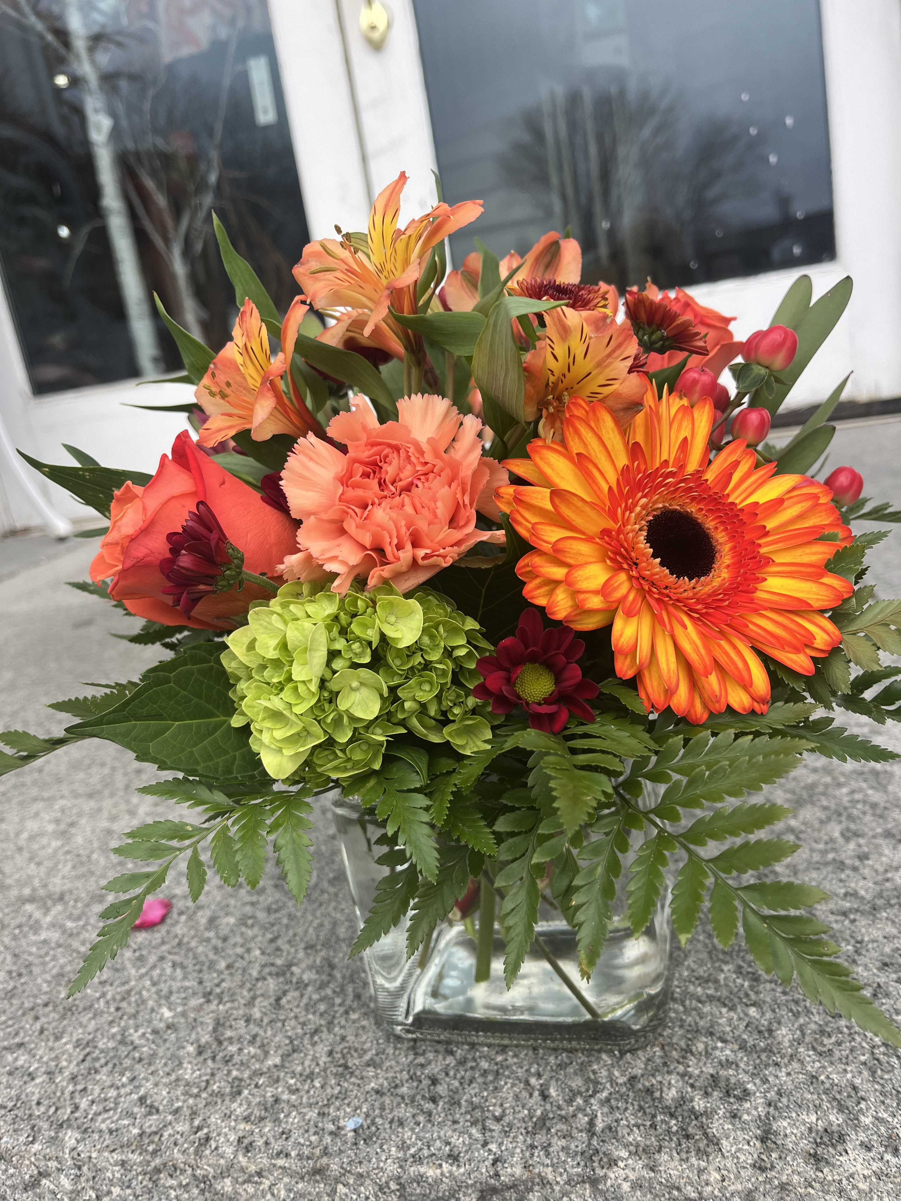 Orange and coral mixed bouquet in a clear glass vase