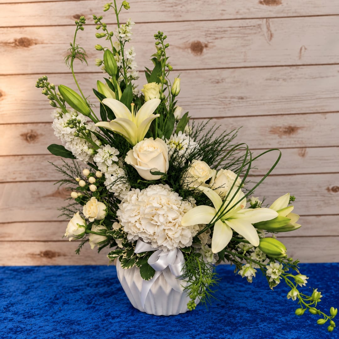 White floral arrangement in a white vase with lilies and roses