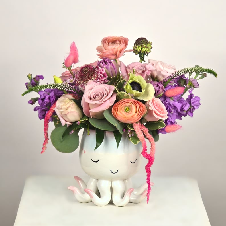 Mixed pink and purple flower arrangement in a white octopus planter