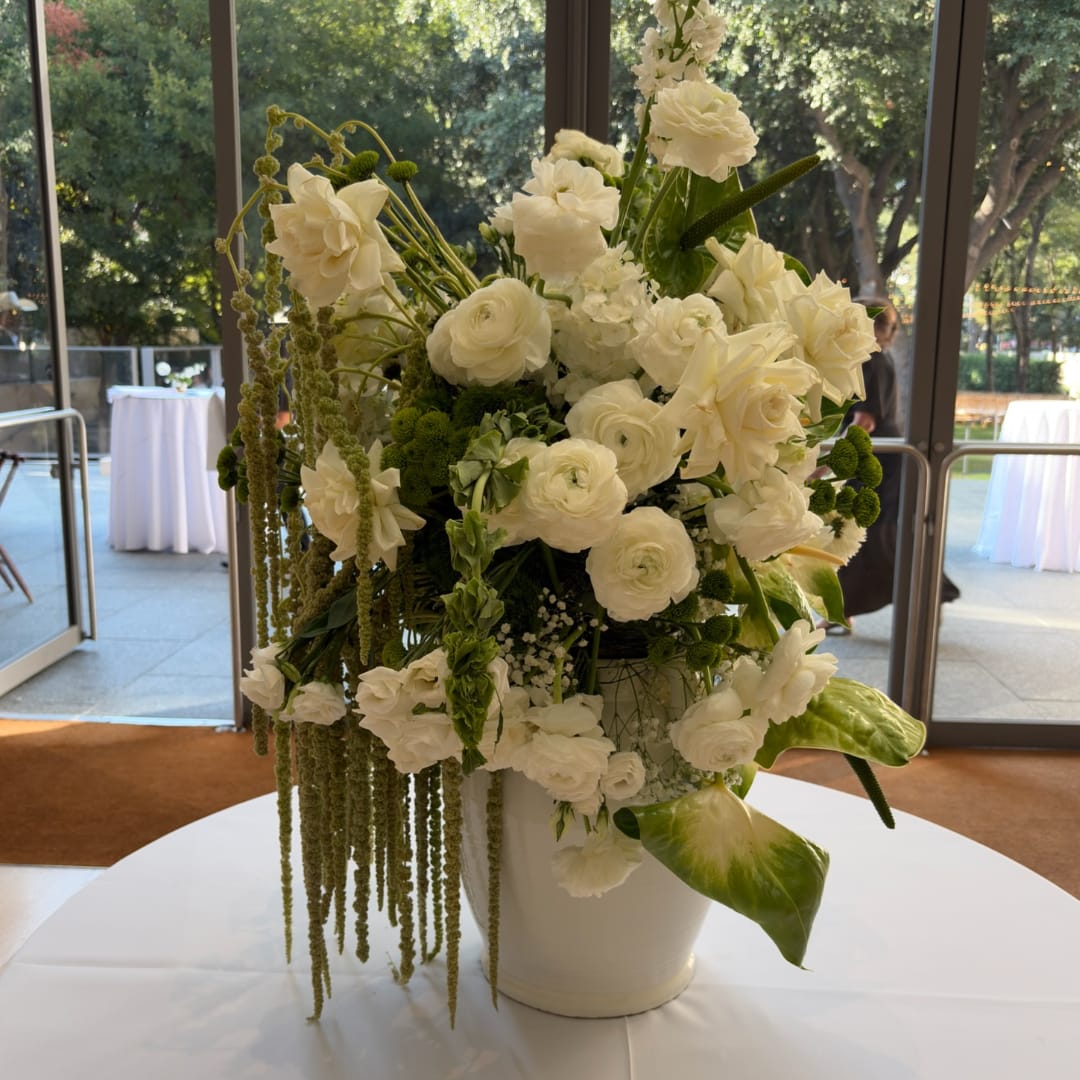 White floral centerpiece in a white vase with trailing greenery