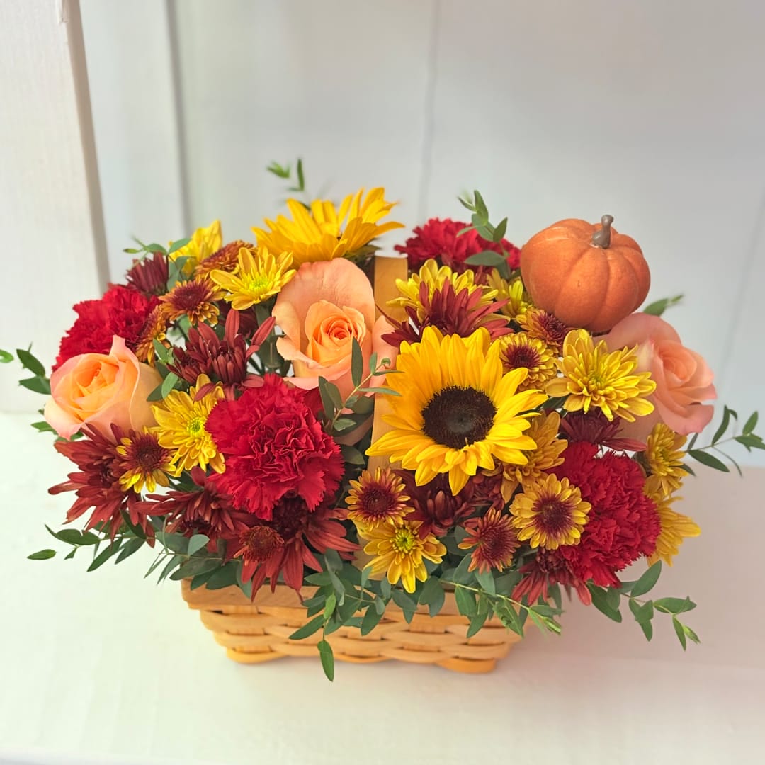 Basket of mixed flowers with roses, sunflowers, and a small pumpkin